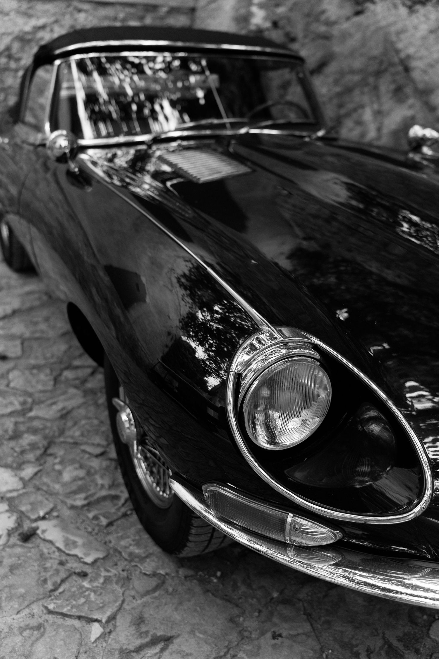Close-up black and white photos showing different angles of a classic Jaguar E-Type sports car's sleek front end design.