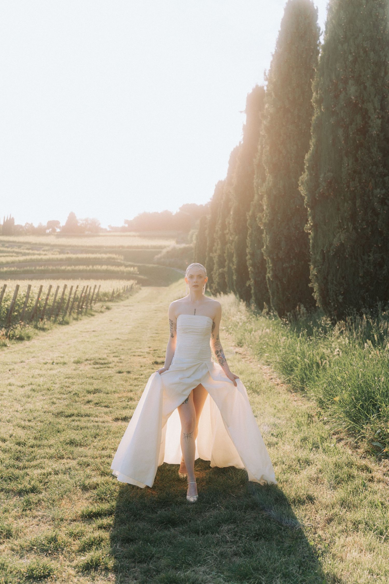 A person in a white dress twirls gracefully in a sunlit field at golden hour with cypress trees in the background.