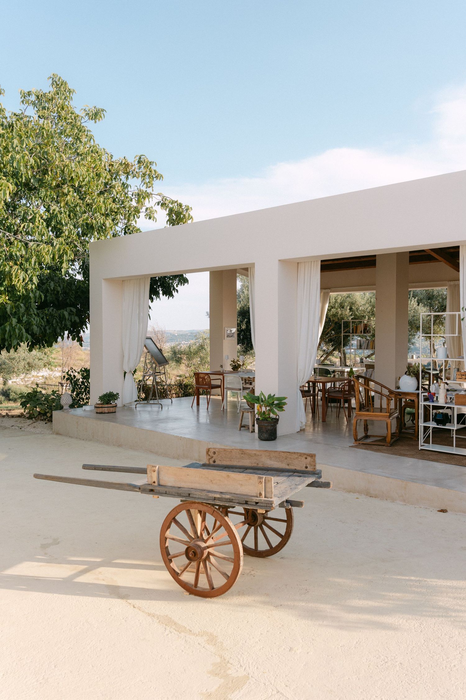 Elegant outdoor terrace with white curtains and a rustic wooden cart overlooking a scenic landscape.