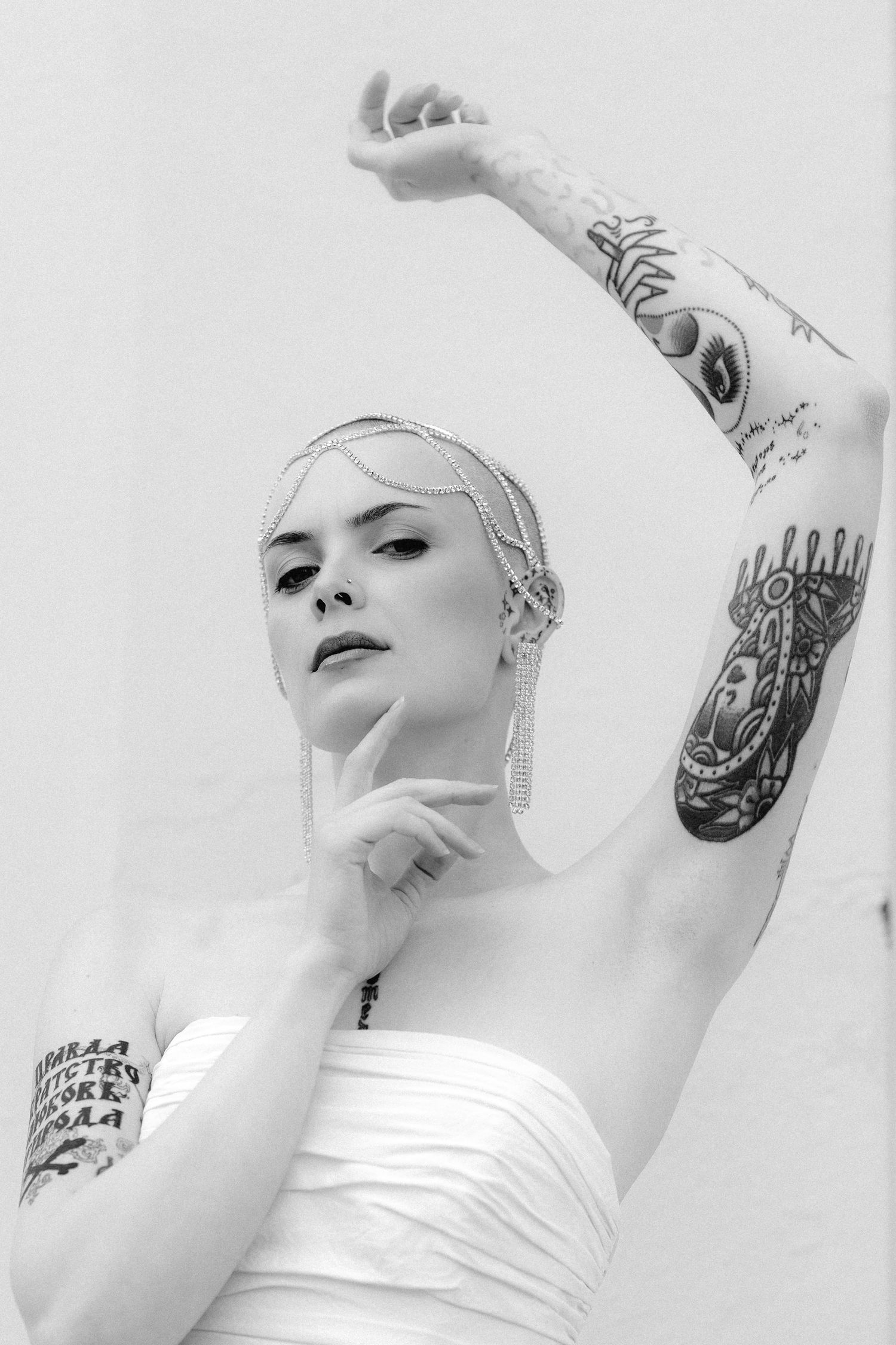 Black and white portrait of person in strapless white dress with visible arm tattoos in artistic pose.