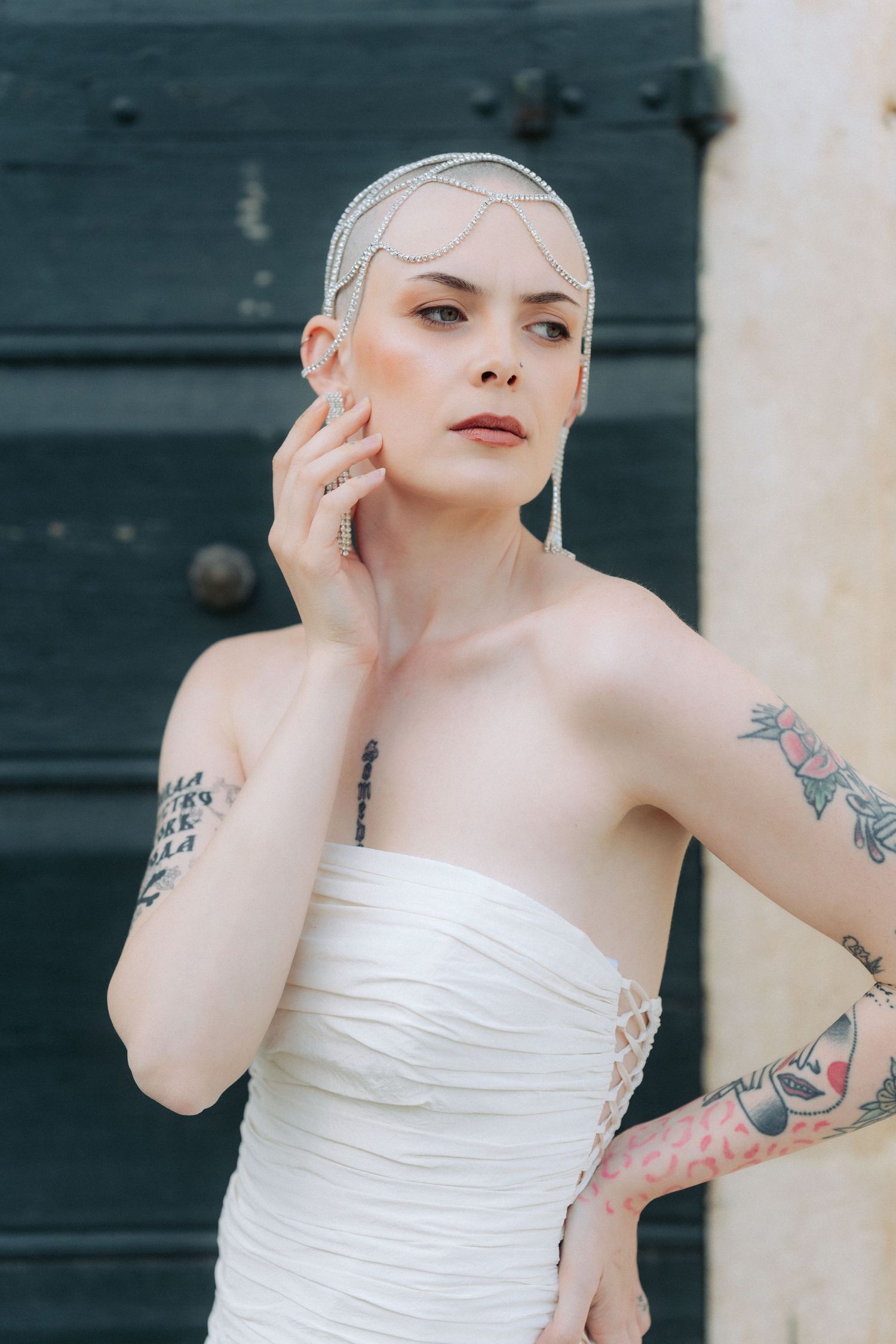 A person in a white strapless dress poses gracefully with visible tattoos on their arms.