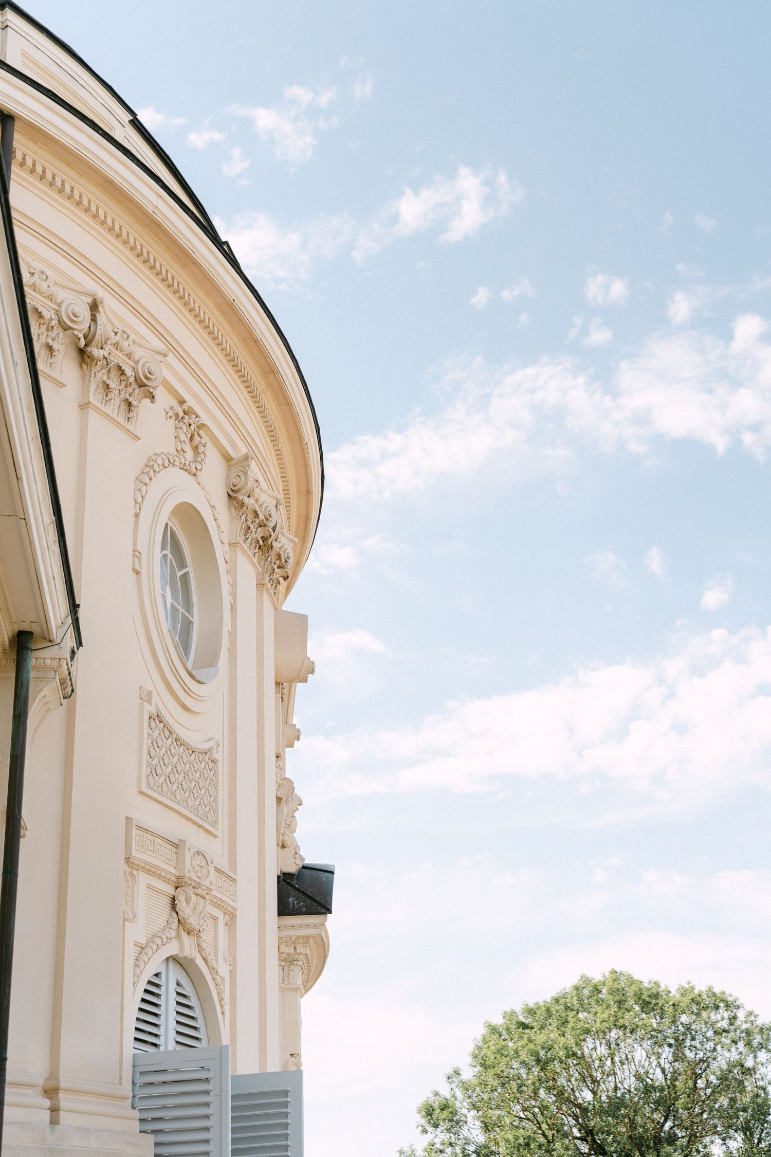 Ornate white architectural detail of a classical building facade with curved walls against a blue sky with clouds. Schloss Solitude