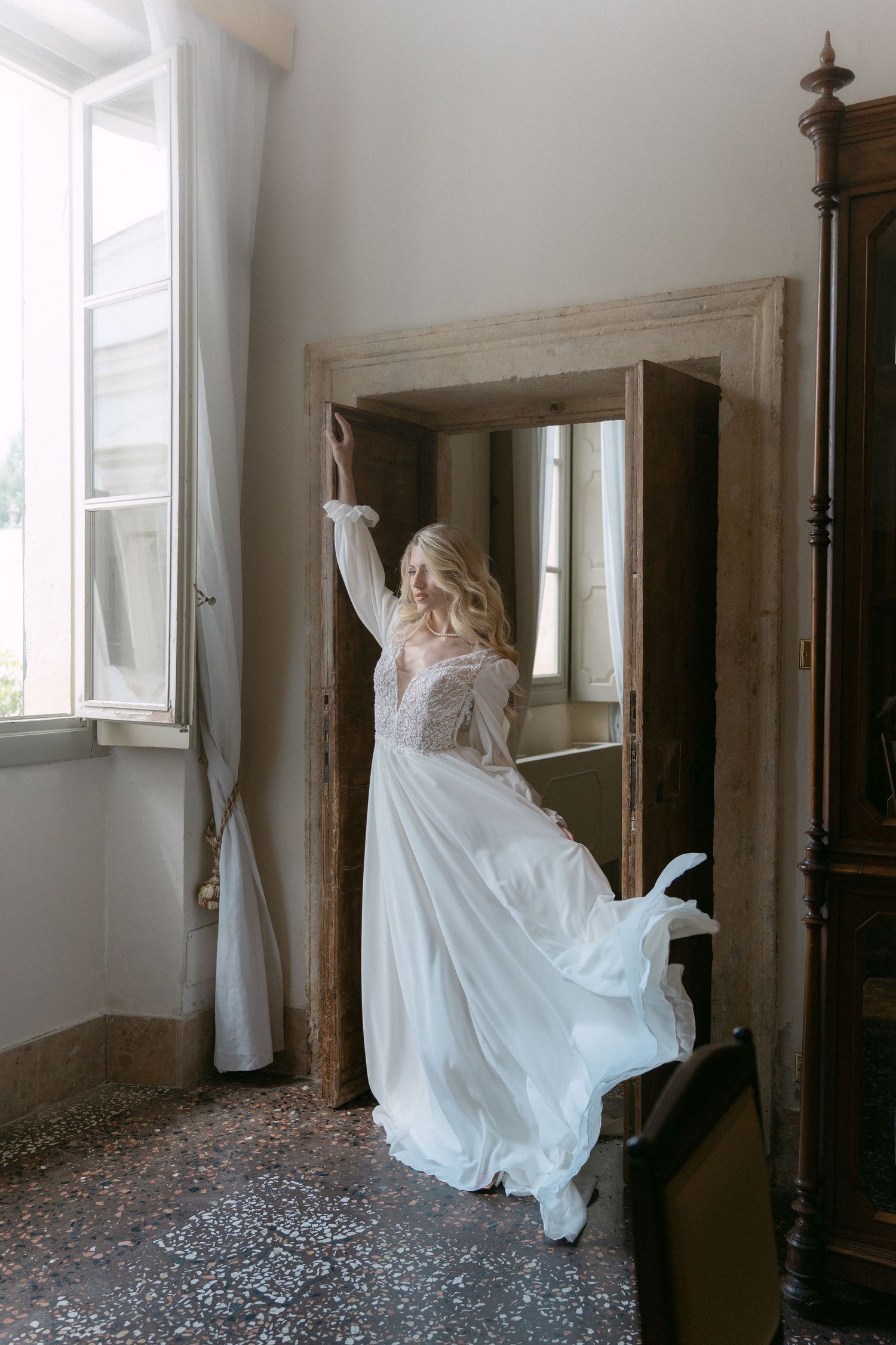A person in a flowing white dress leaps gracefully through an ornate doorway in a bright interior space. Wedding Verona