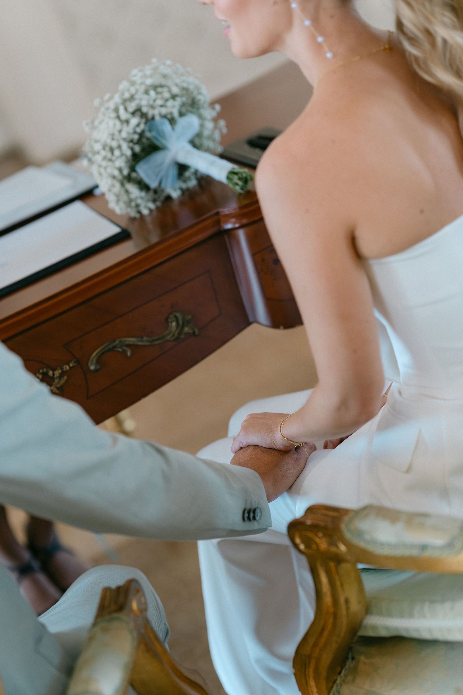A close-up of a bride in a white wedding dress holding hands with someone in a gray suit sleeve during a ceremony. Schloss Solitude