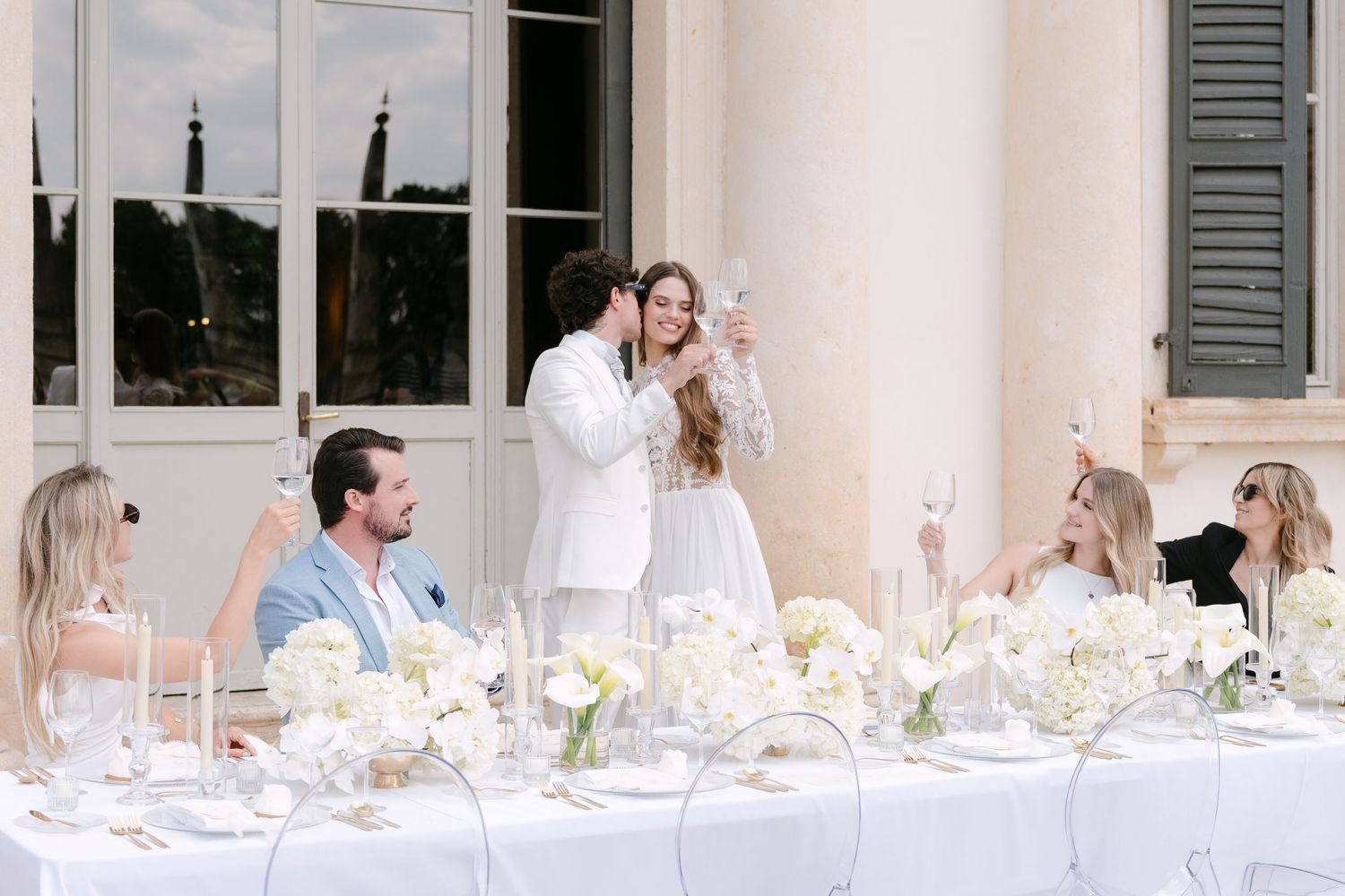 A long table is set for an elegant outdoor wedding reception with white linens and floral centerpieces. Villa Mosconi Bertani