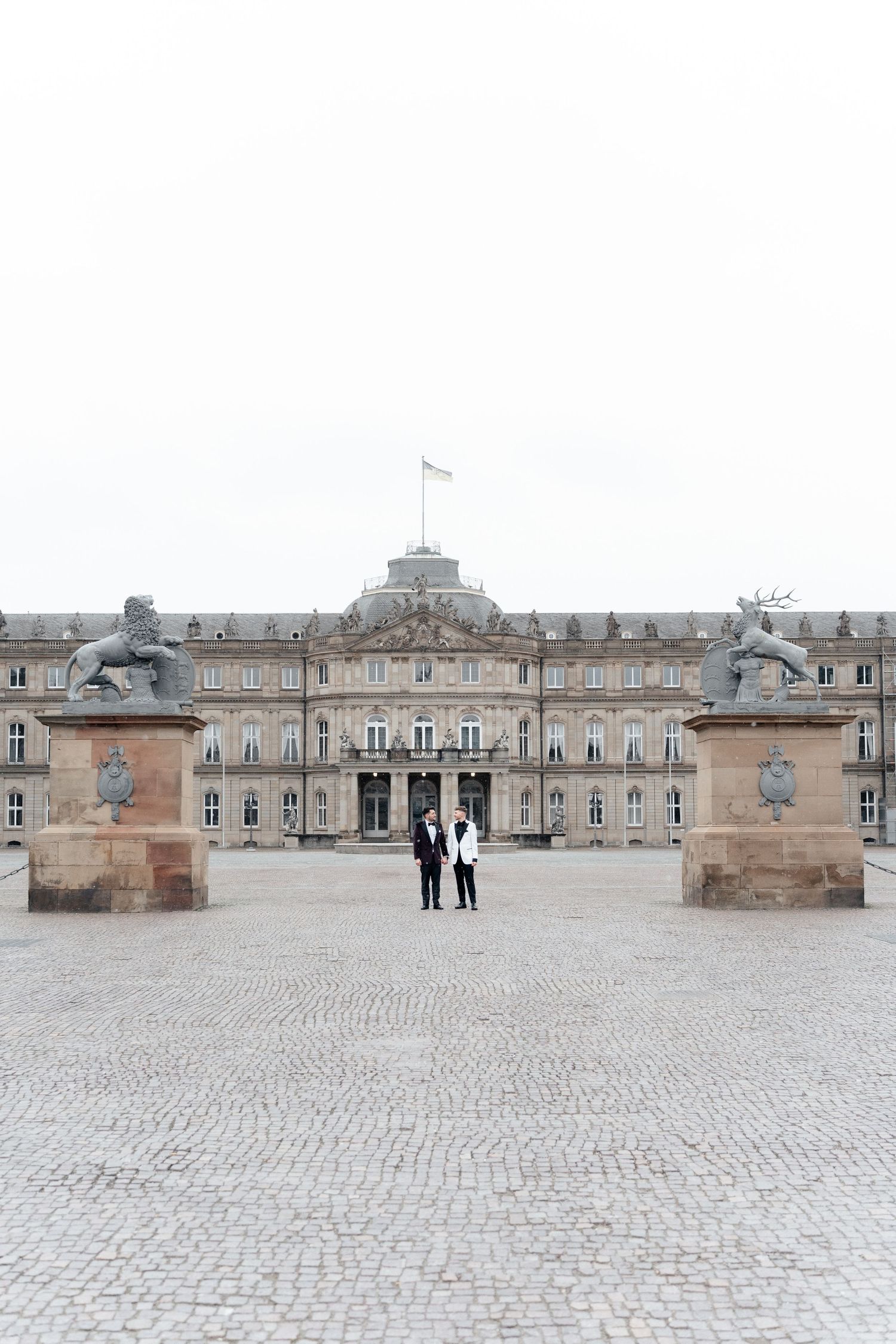 Elegant historic palace with symmetrical architecture and stone statues guarding its grand entrance in Stuttgart, Germany.