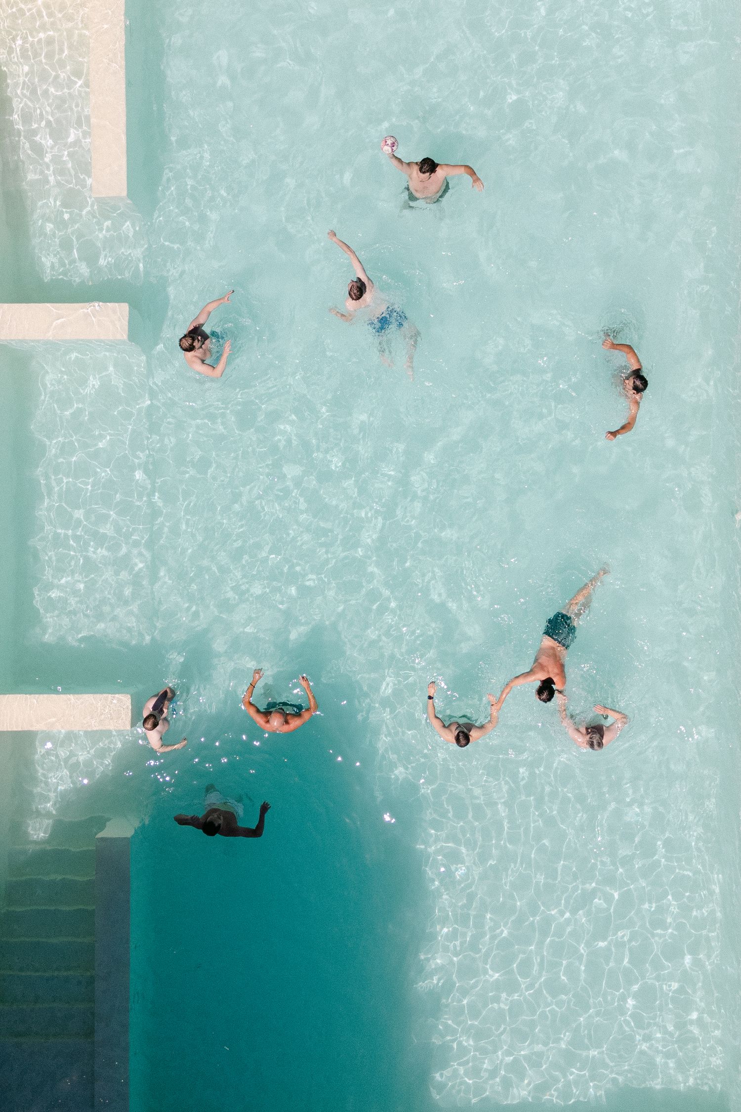Aerial view of swimmers forming a circle pattern in a turquoise pool, viewed from above near pool steps.