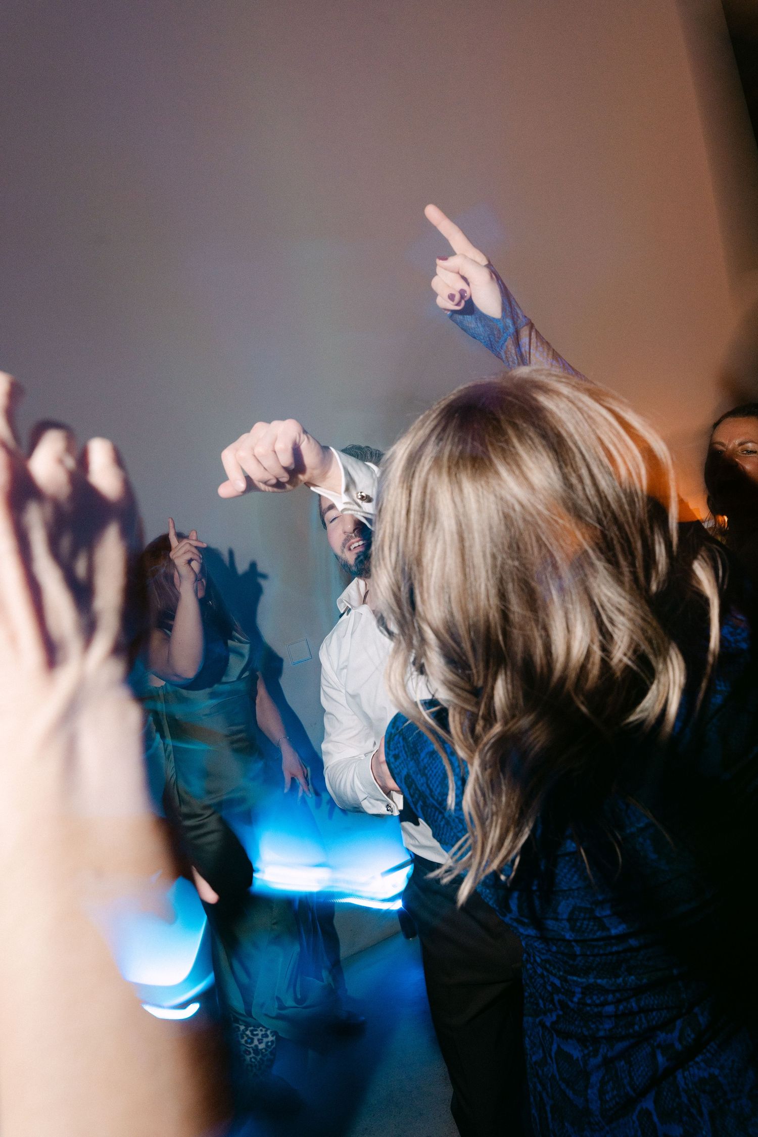 People dancing at a party with blue stage lights and hands raised in the air.