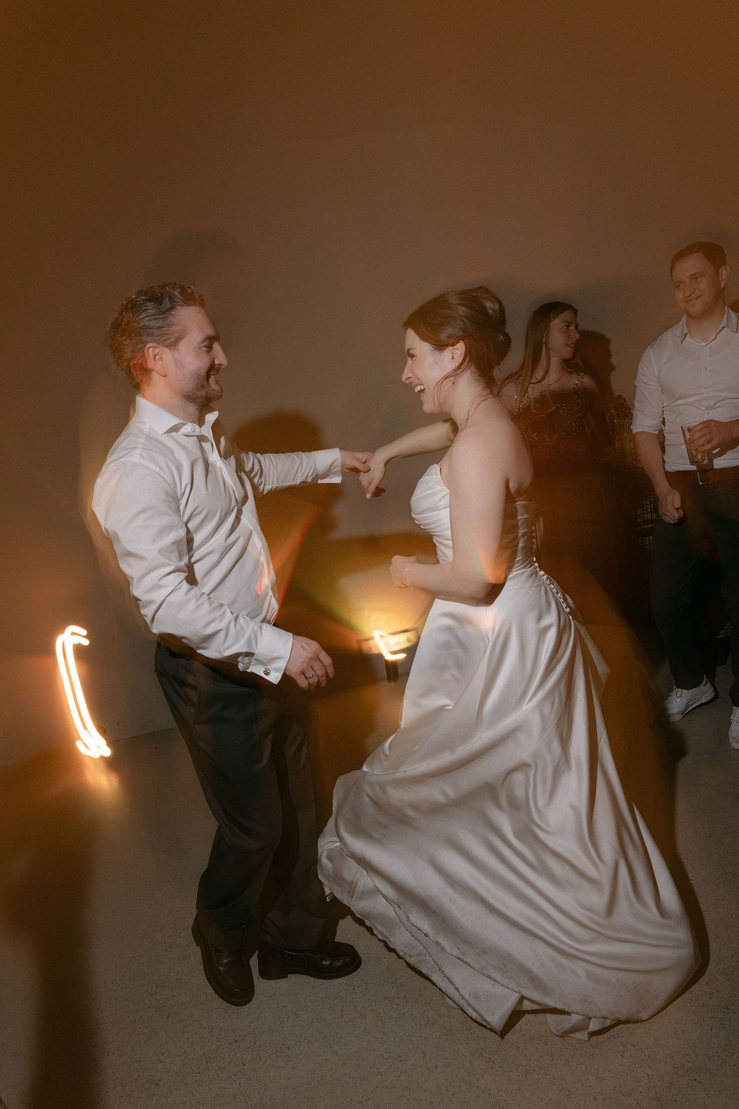 Bride and groom share a joyful first dance together at their wedding reception in warm golden lighting.
