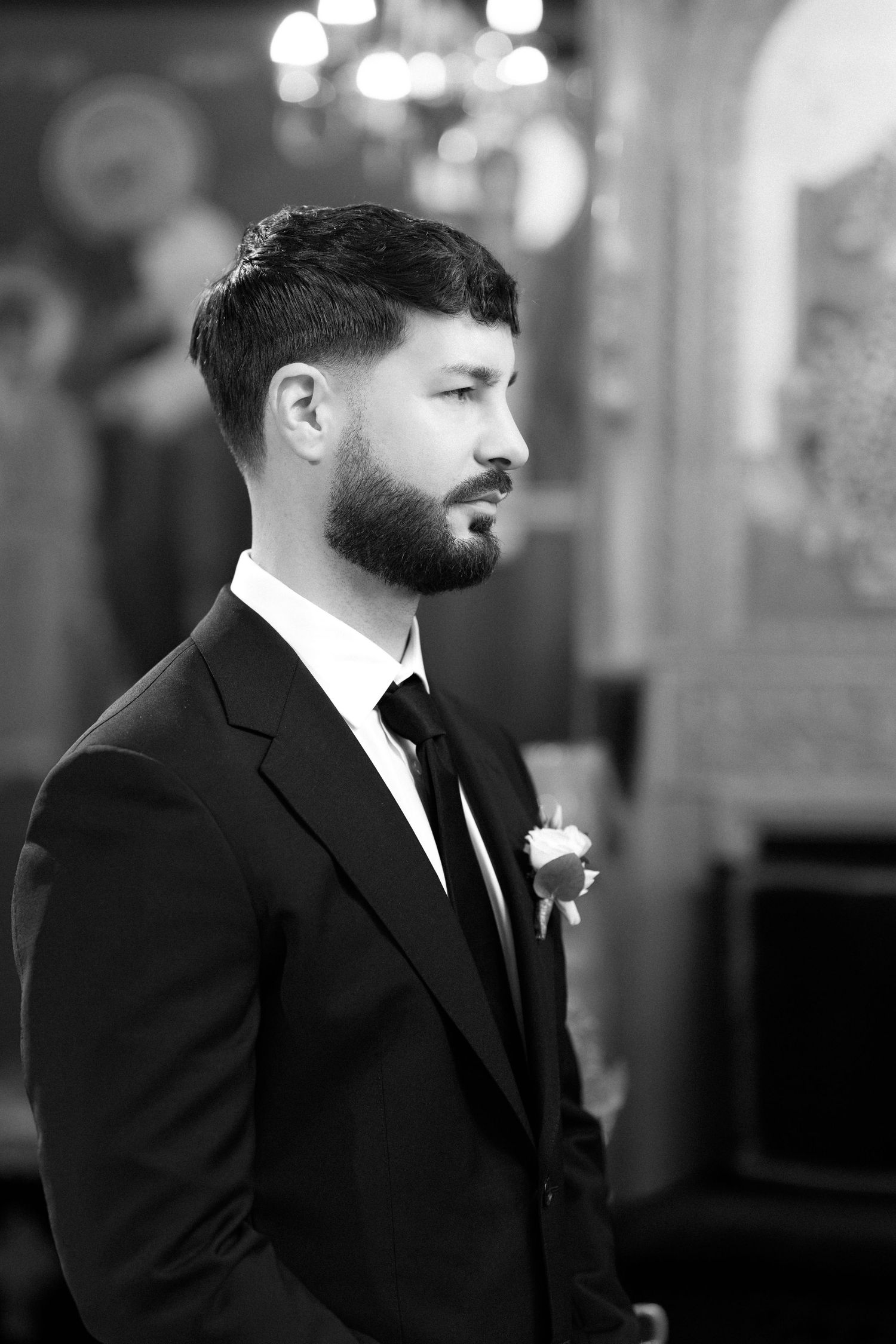 Elegant groom in black tuxedo with boutonniere and bow tie, black and white portrait photo.