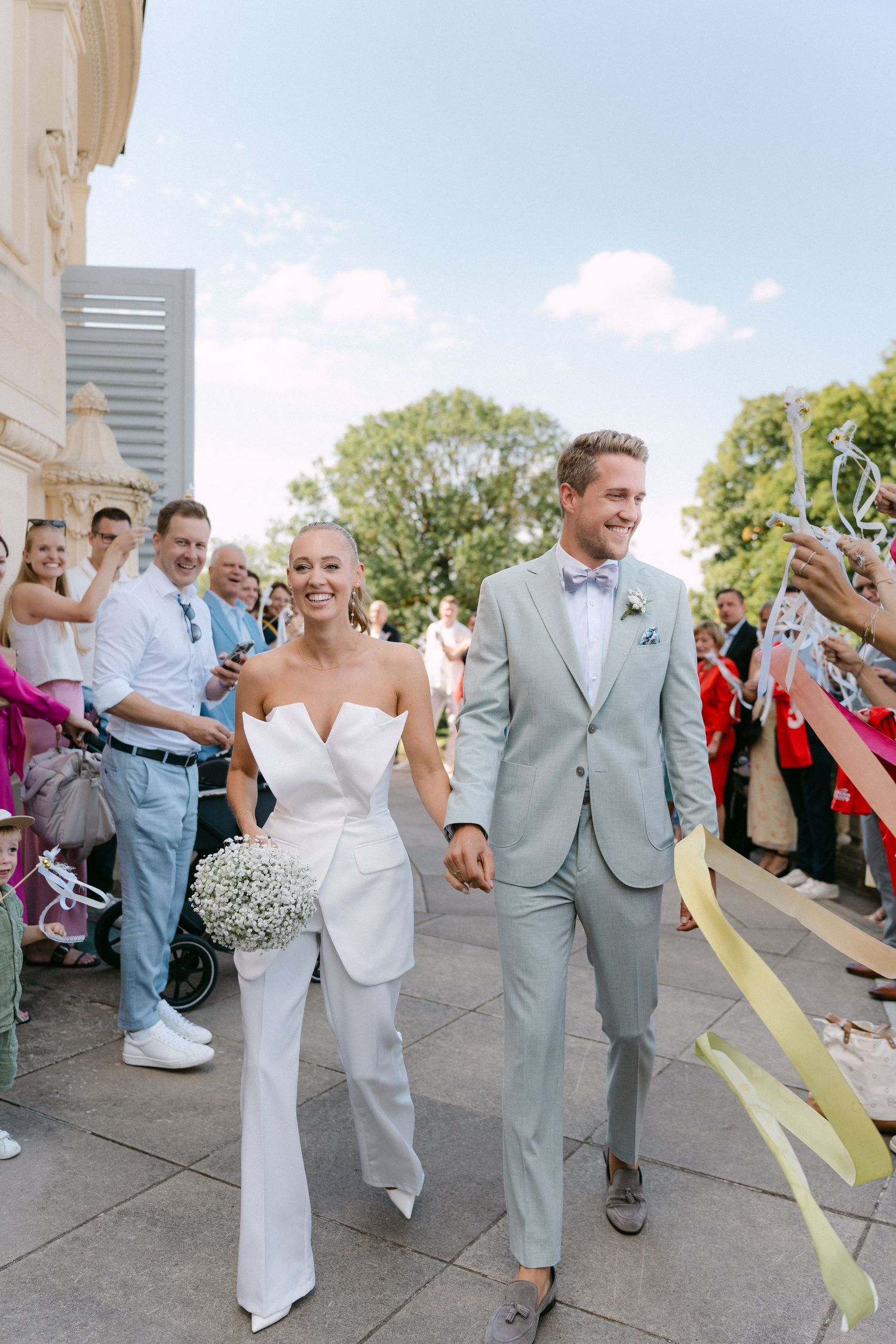 Wedding party celebrates with colorful streamers as they walk together on a sunny day outside a building. Schloss Solitude