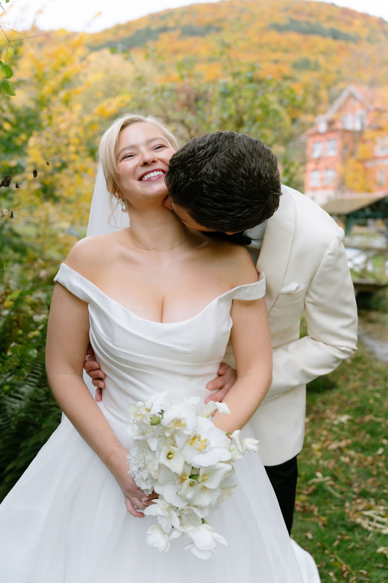 A couple shares a romantic moment on their wedding day against an autumn backdrop with colorful fall foliage.