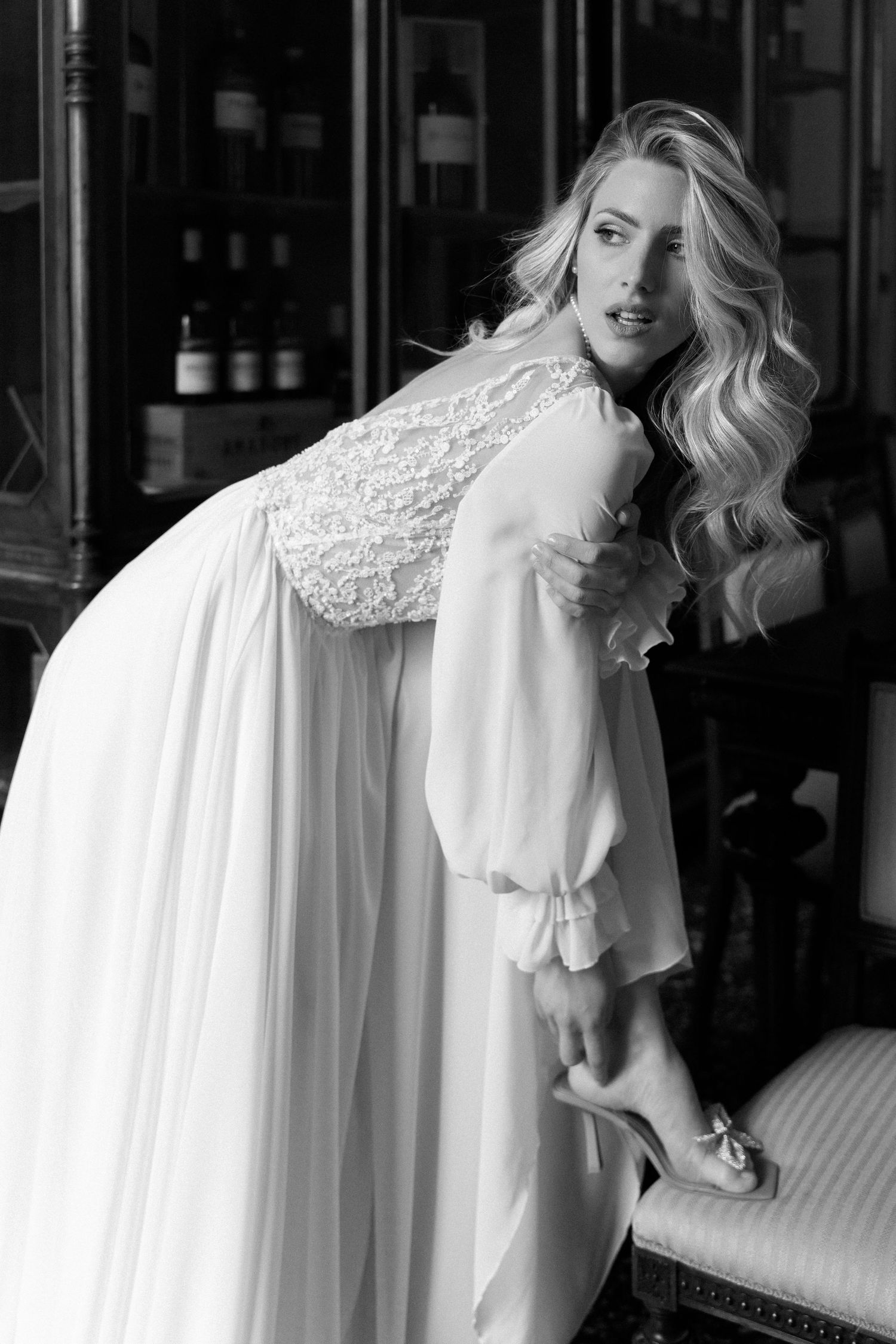 A black and white fashion portrait of someone wearing a flowing white dress with a lace collar against a dark background. Wedding Verona