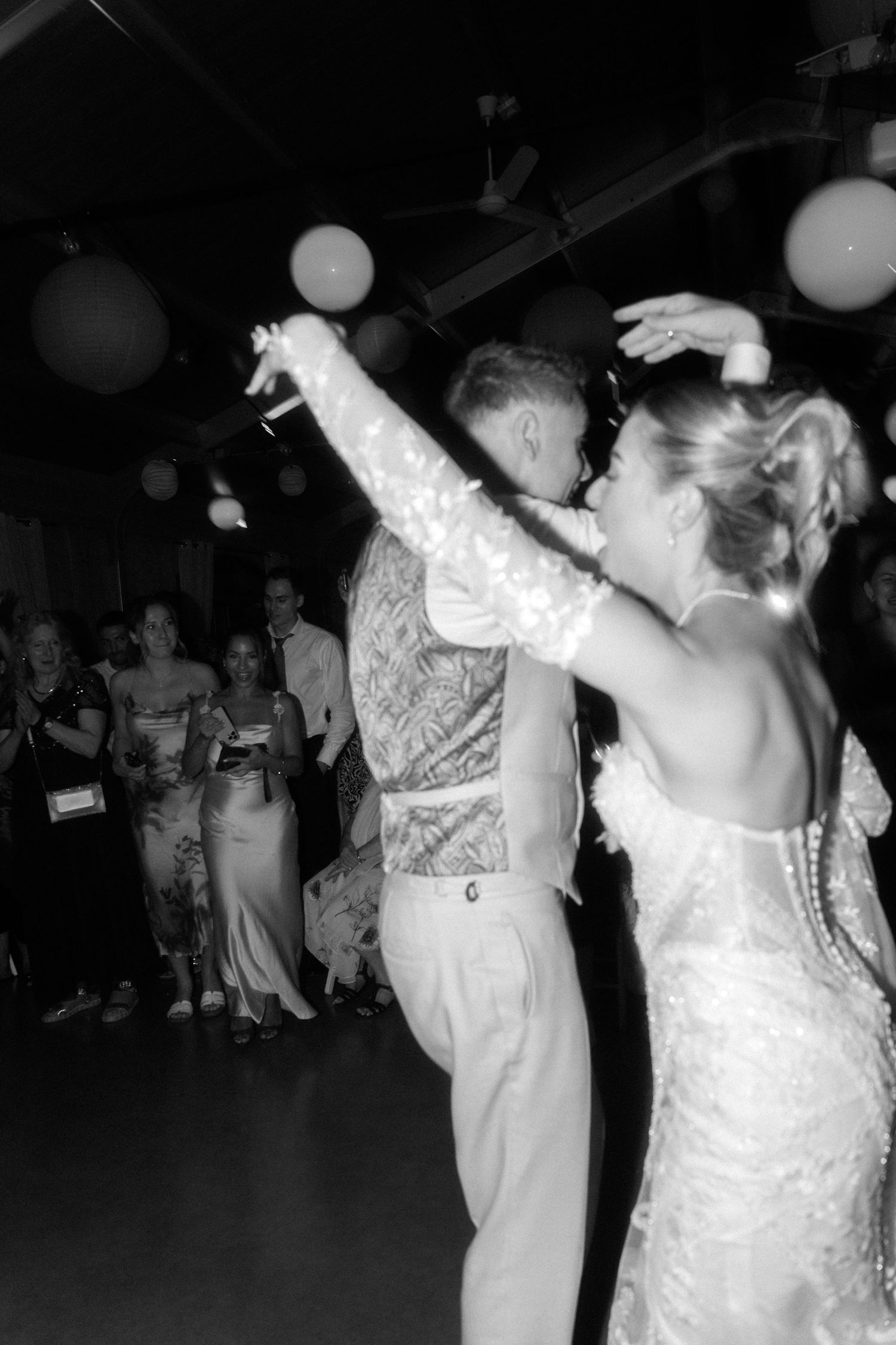 A couple dances energetically at a wedding reception with paper lanterns decorating the ceiling above.