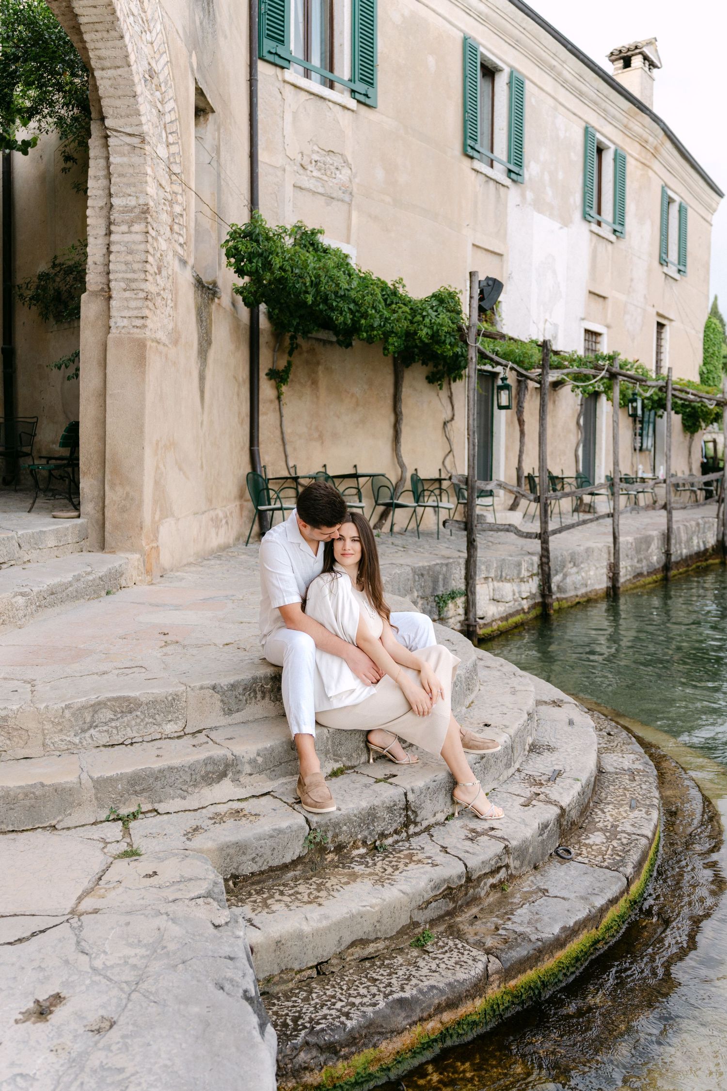 A series of photos showing someone sitting along a stone canal wall with turquoise shuttered buildings in Venice, Italy.