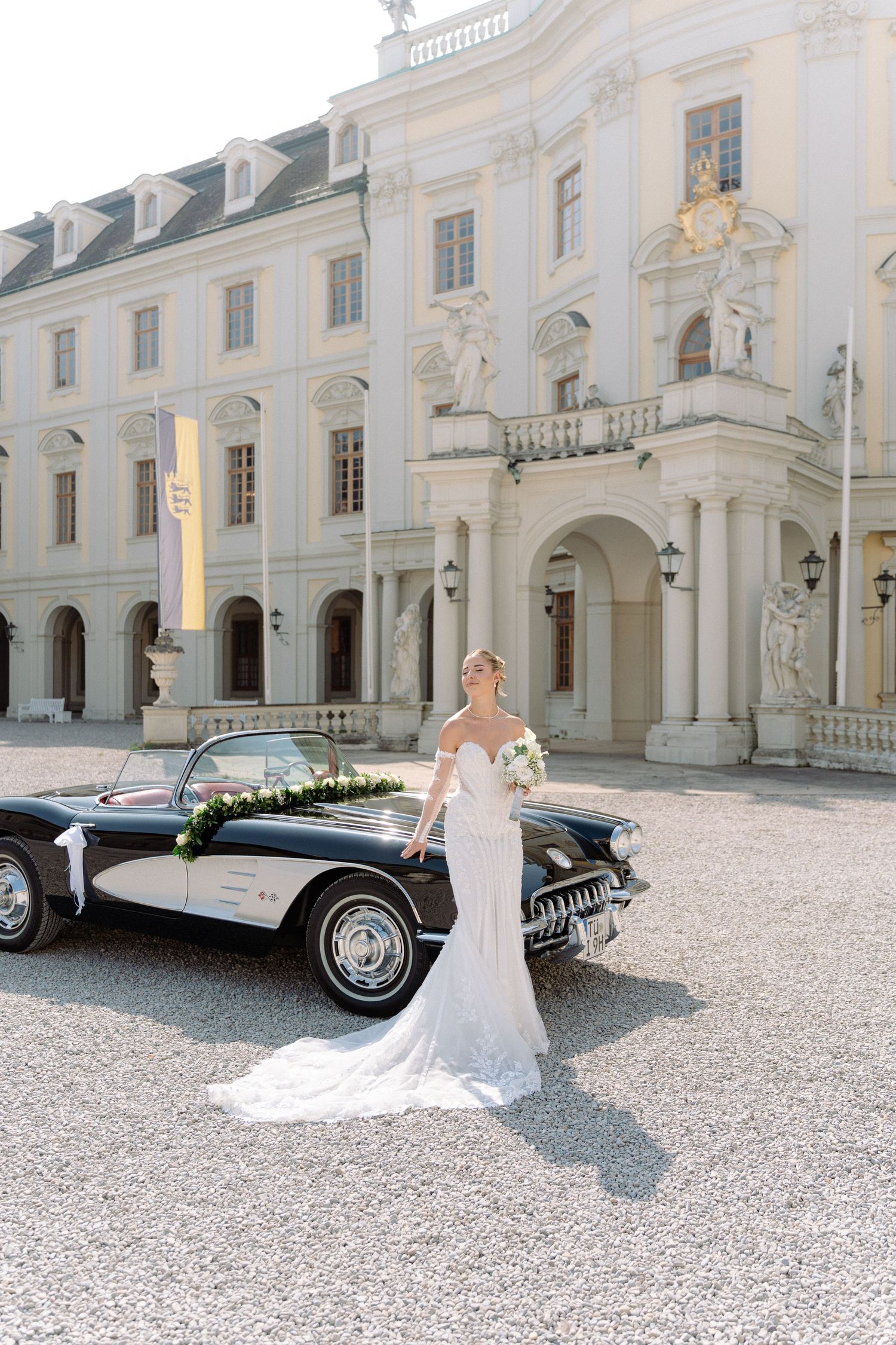 Classic black vintage car parked in front of an elegant white palace with ornate architecture and gravel courtyard. Schloss Ludwigsburg