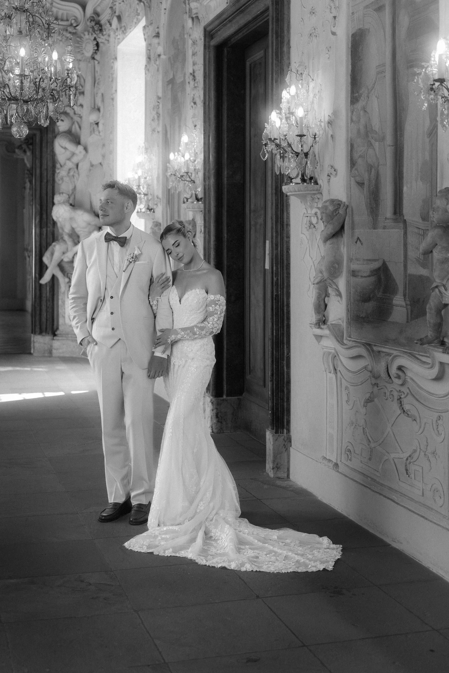 A black and white photo series showing a couple in formal wedding attire posing in an ornate hallway with chandeliers. Schloss Ludwigsburg