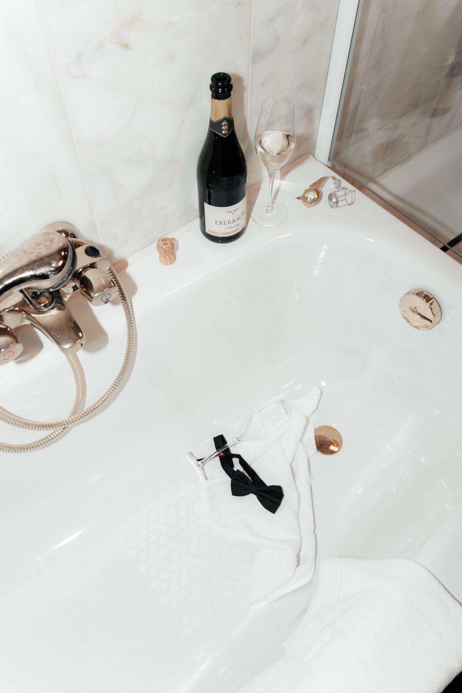 Luxurious bathtub setup with champagne bottle, wine glass, and black tie bow accessory creating an elegant spa atmosphere.