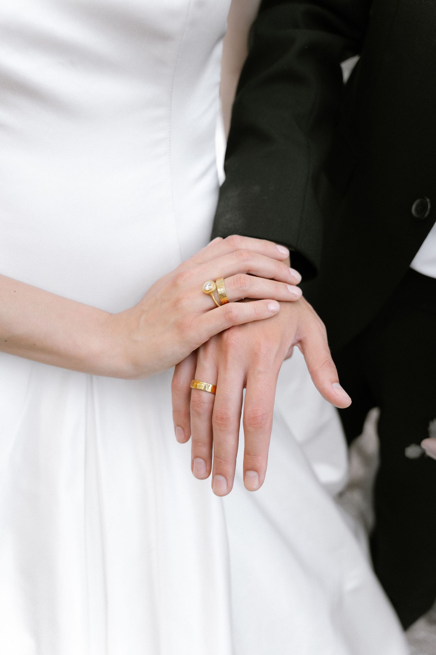 Bride and groom hands together showing gold wedding rings, white bridal gown and black suit.