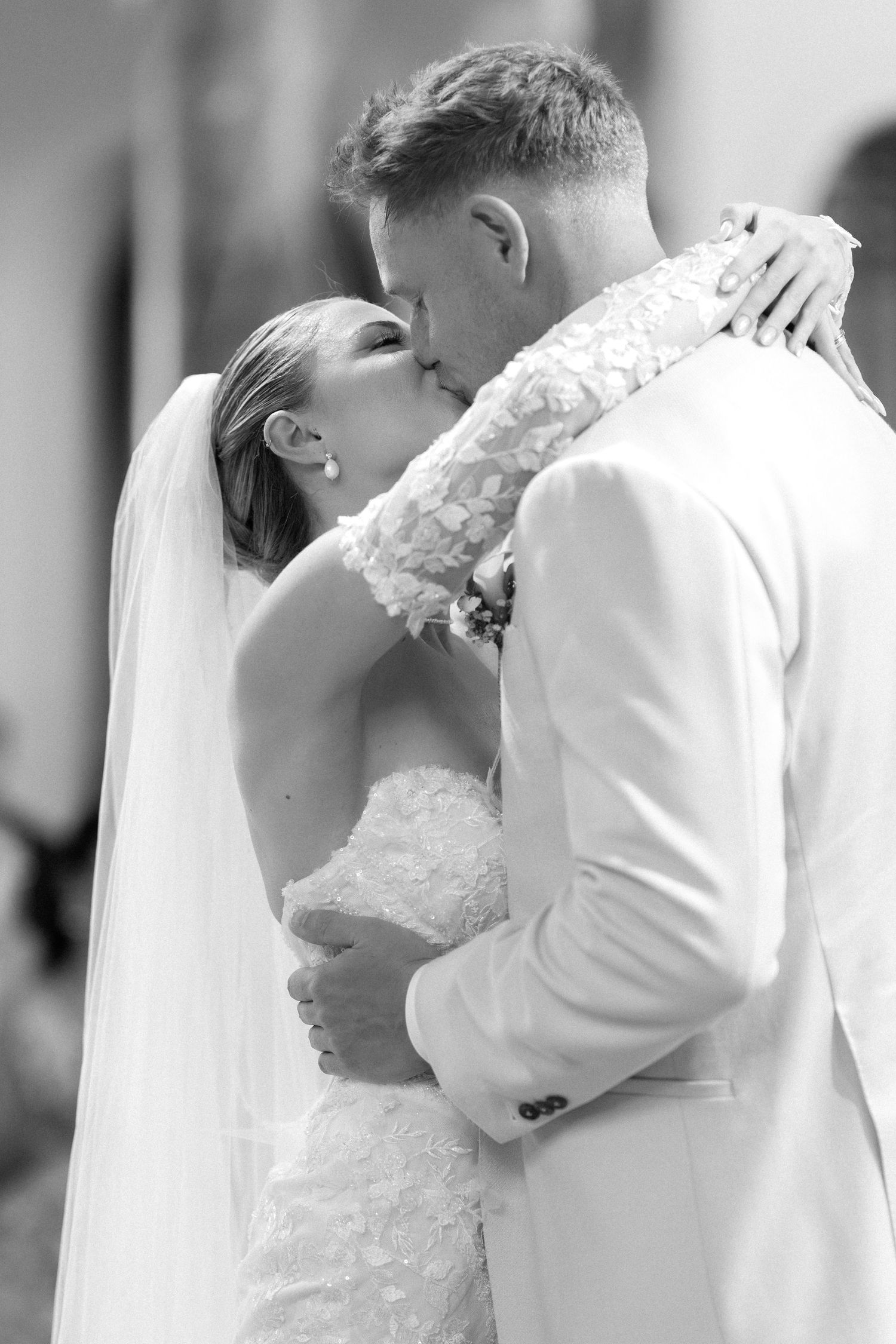 A romantic black and white photo series showing a couple in wedding attire sharing their first kiss as newlyweds.