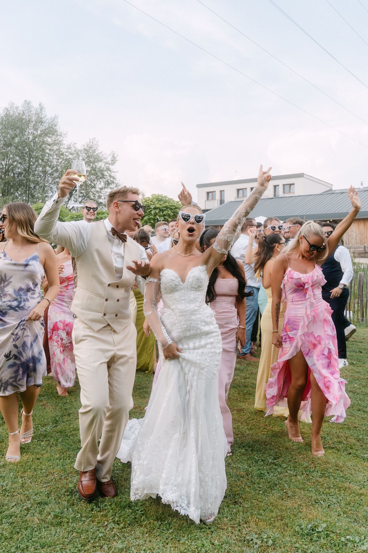 Wedding guests celebrate and dance together outdoors on a grassy lawn during a summer reception party.