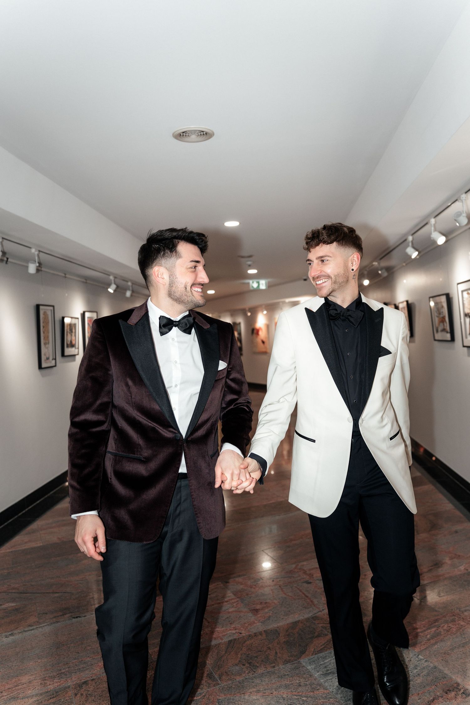 Two people in formal attire sharing a happy moment as they walk down a hallway holding hands.