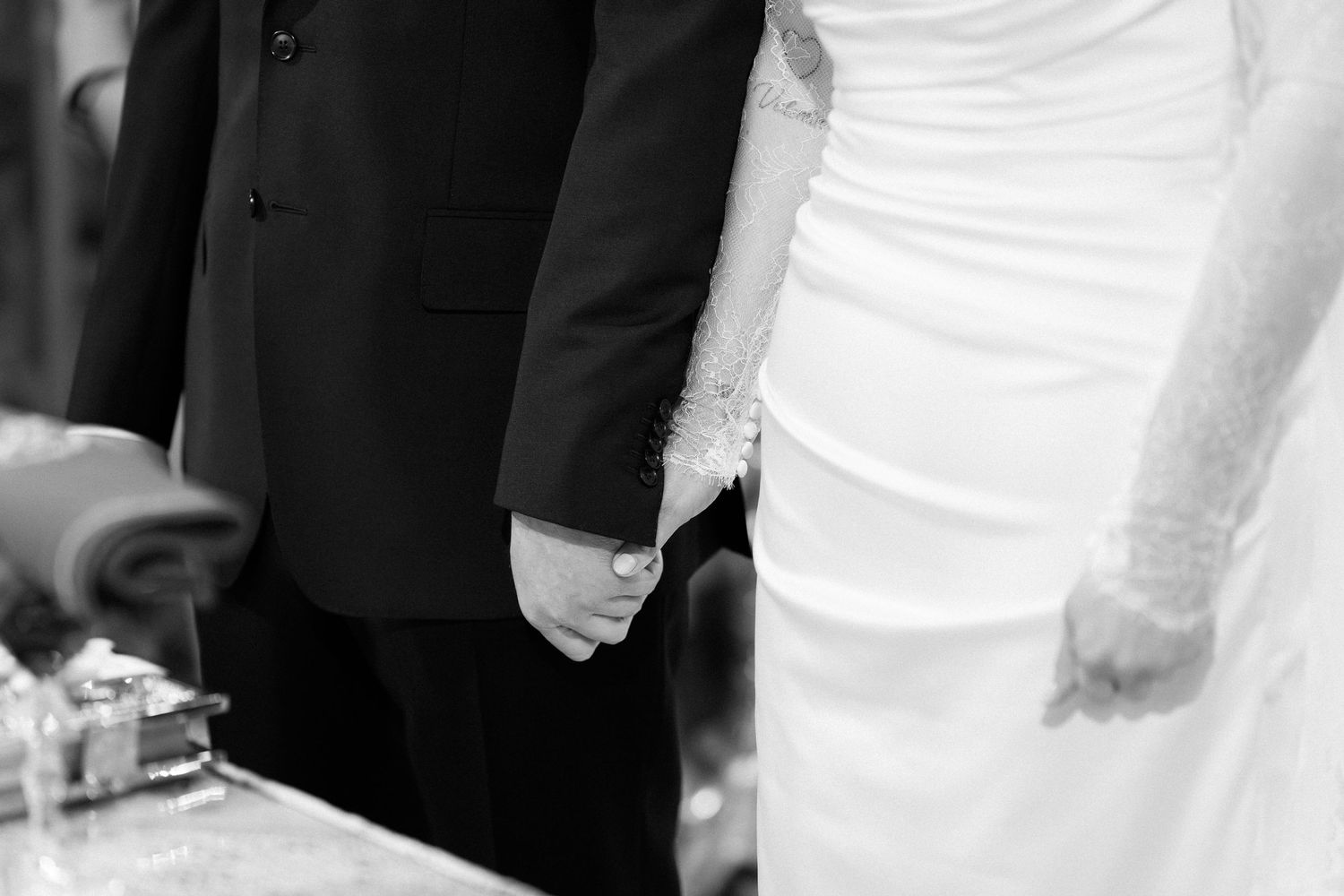 Black and white photo of bride and groom holding hands at wedding ceremony altar.