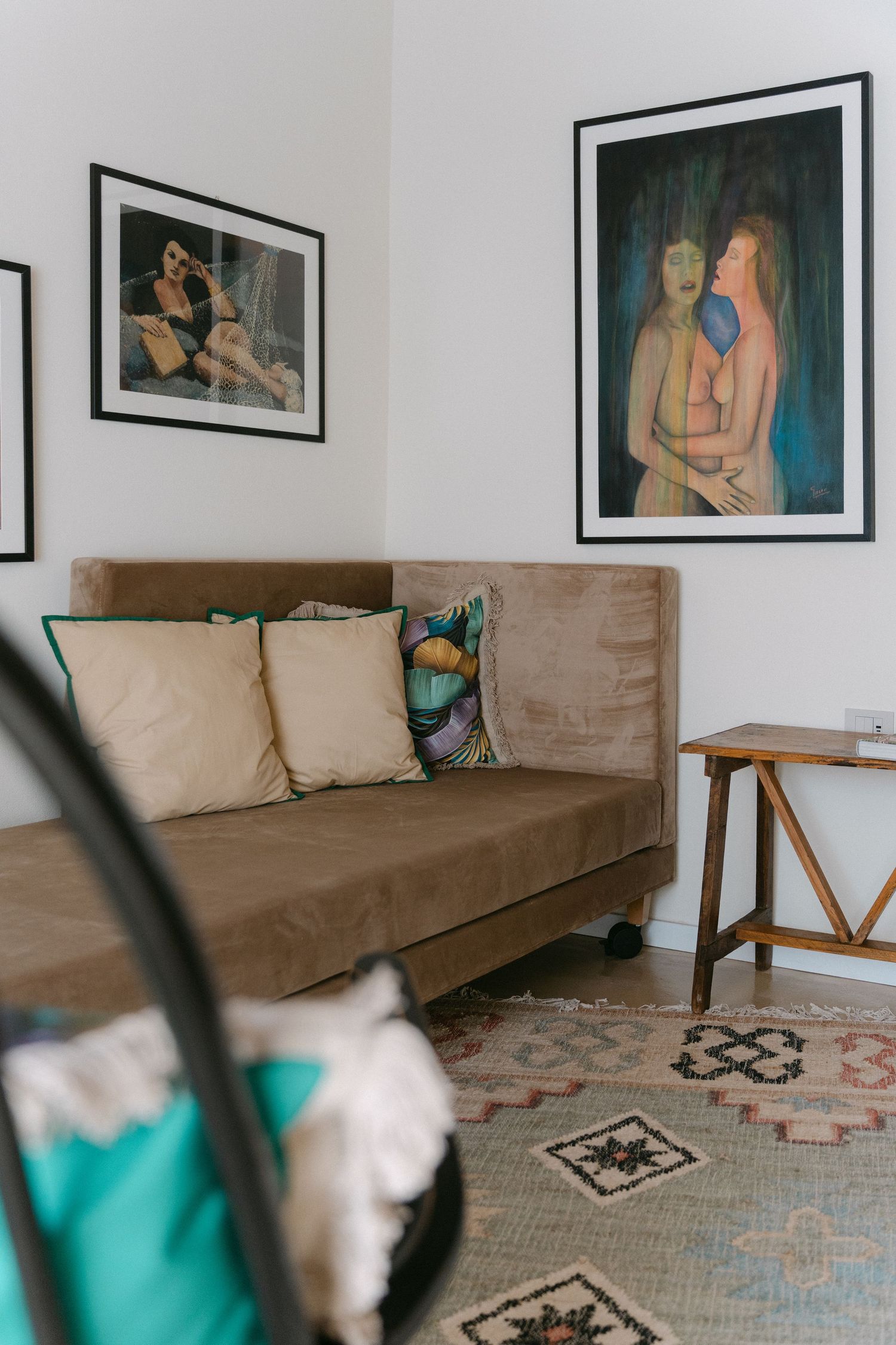 A living room with a brown couch, patterned rug, and framed artwork on white walls.
