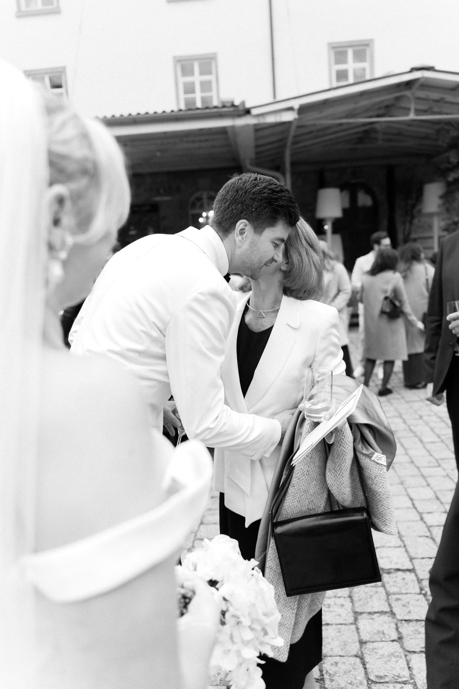 Romantic wedding moment captured in black and white as couple shares an intimate kiss on cobblestone courtyard.