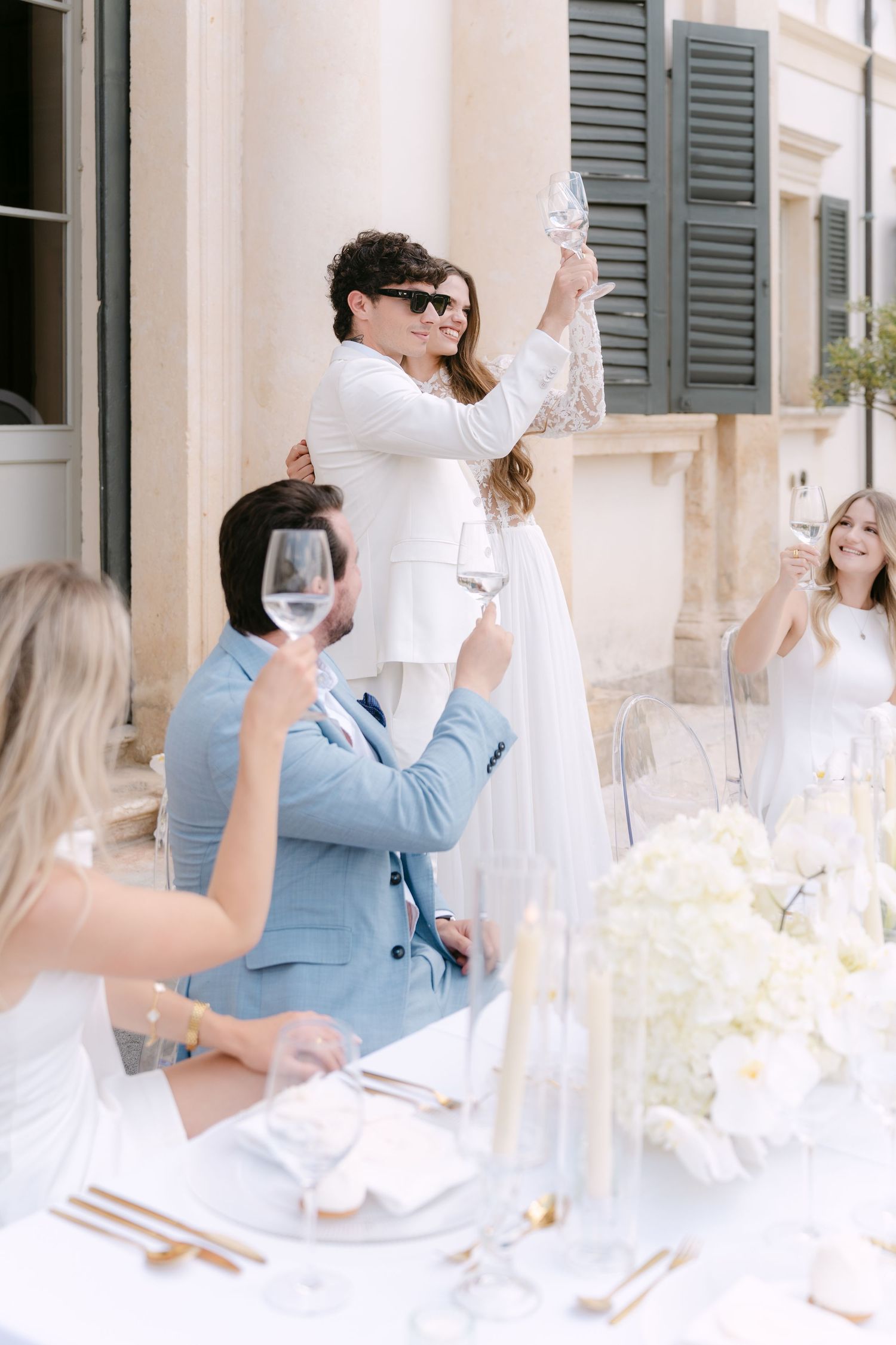People in white and blue attire gather around an elegant table setting for a special celebration. Villa Mosconi Bertani