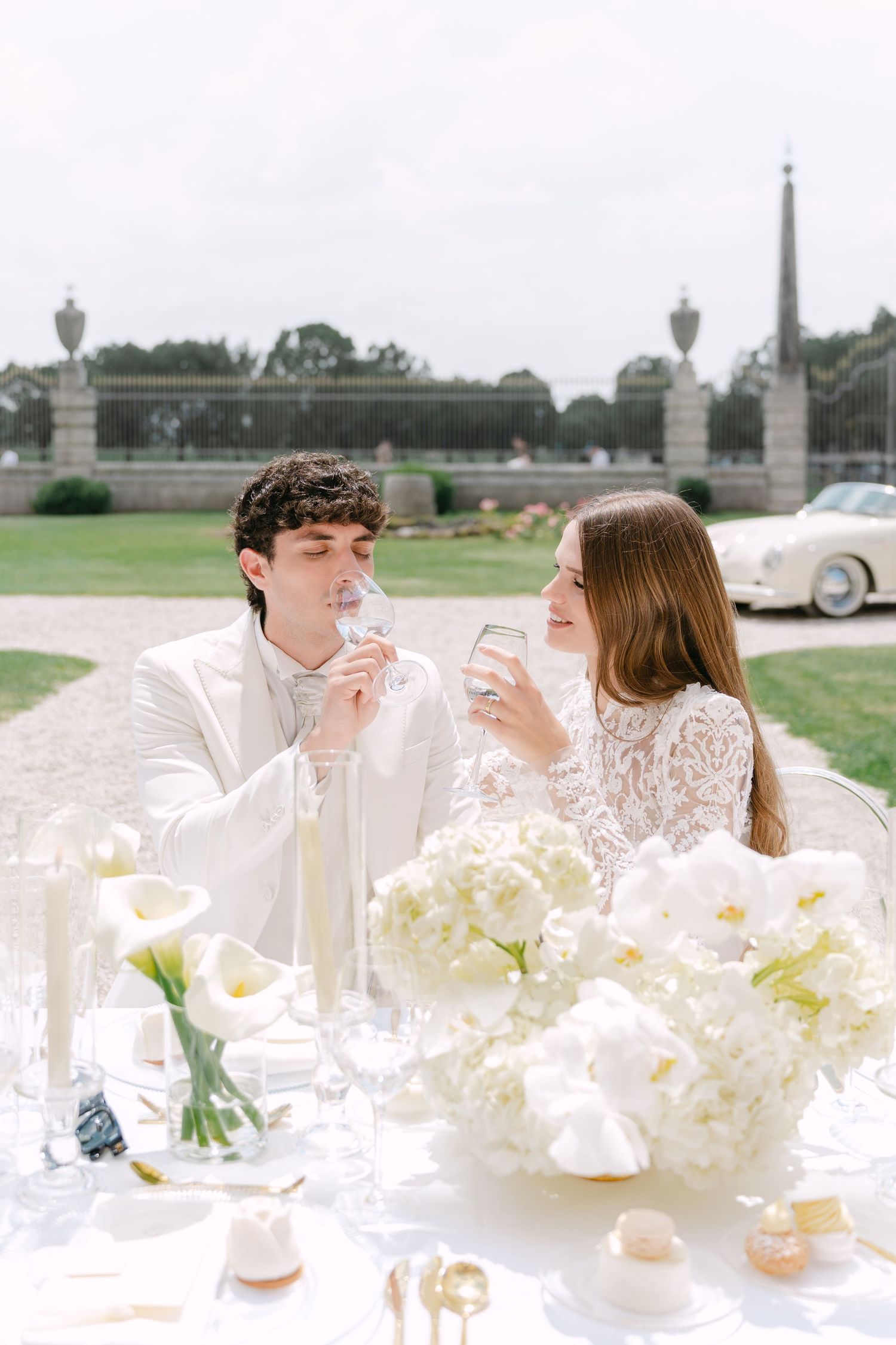 A couple shares drinks at an elegant outdoor table with white flowers and the Eiffel Tower visible in the background. Villa Mosconi Bertani