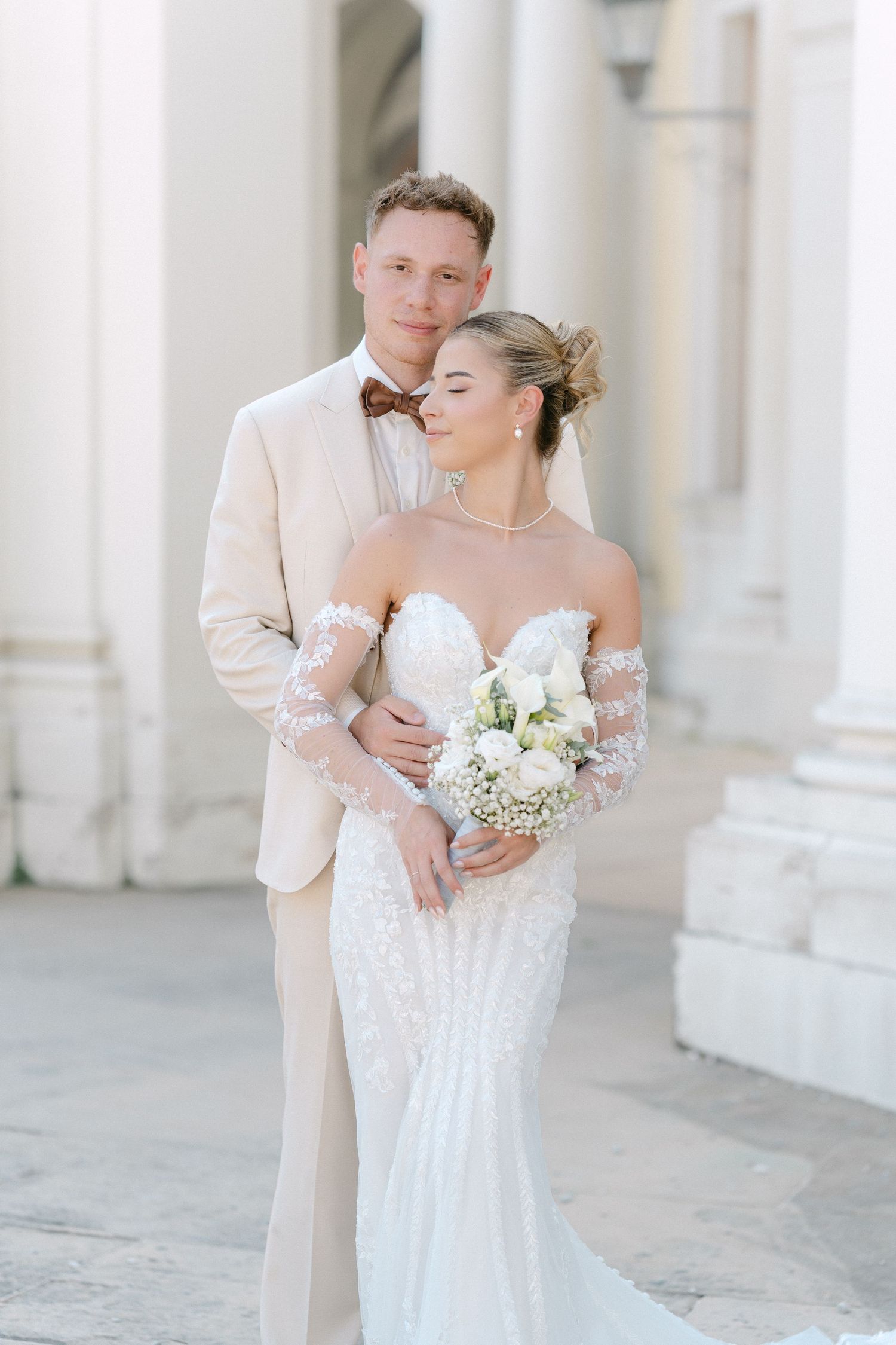 A bride and groom share romantic moments in an elegant white colonnade setting during their wedding photoshoot. Schloss Ludwigsburg