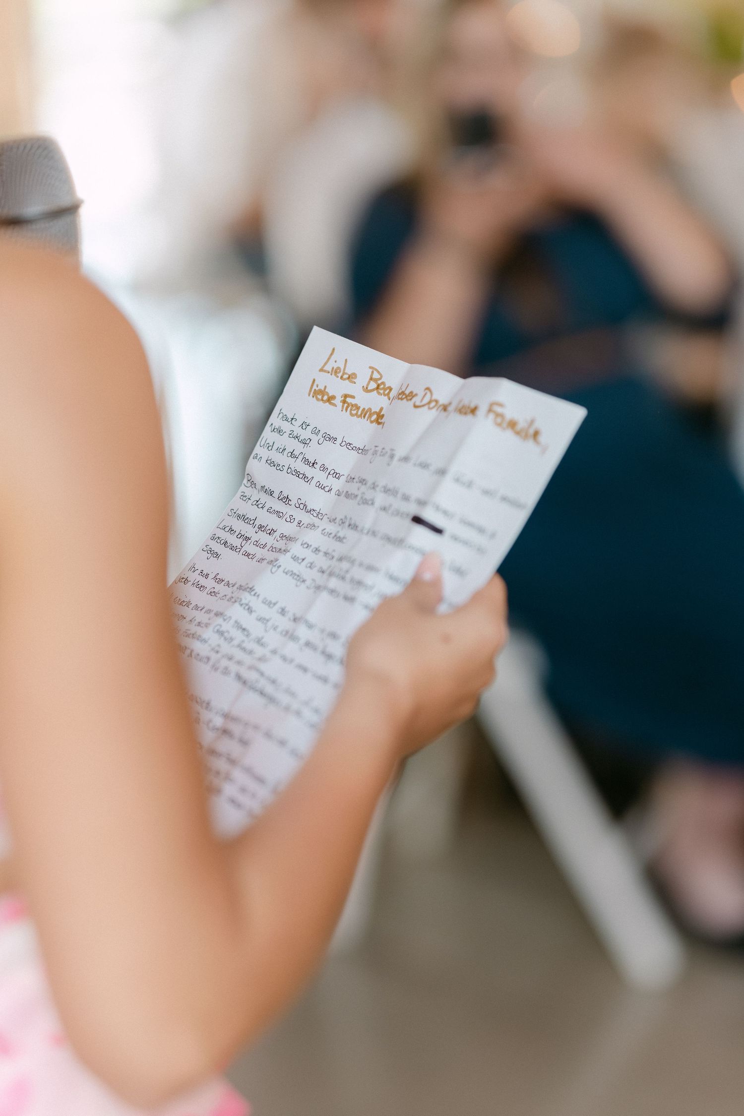 Close-up view of hands holding handwritten vows or love letter on white paper during wedding ceremony.