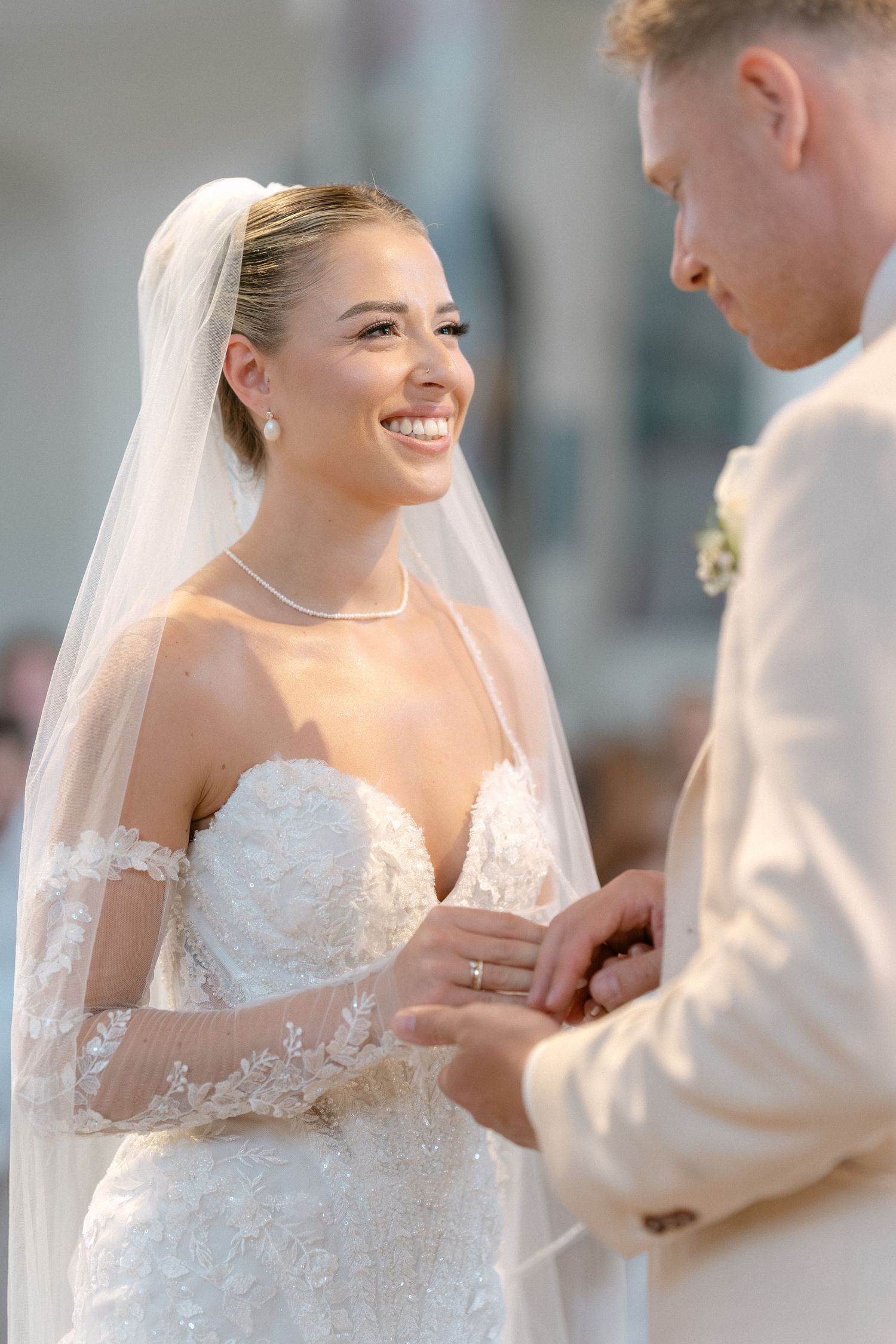 A joyful moment during a wedding ceremony as the bride and groom exchange rings in elegant white attire.