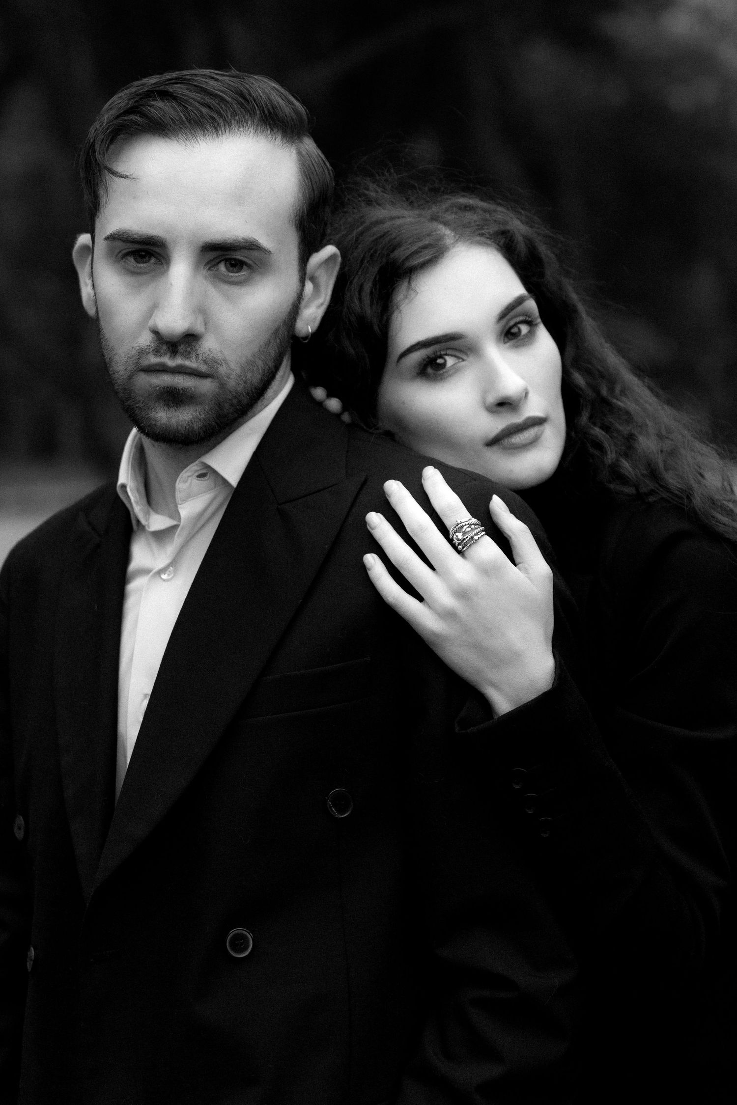 A romantic black and white portrait of a couple in formal attire posed together against a dark background.