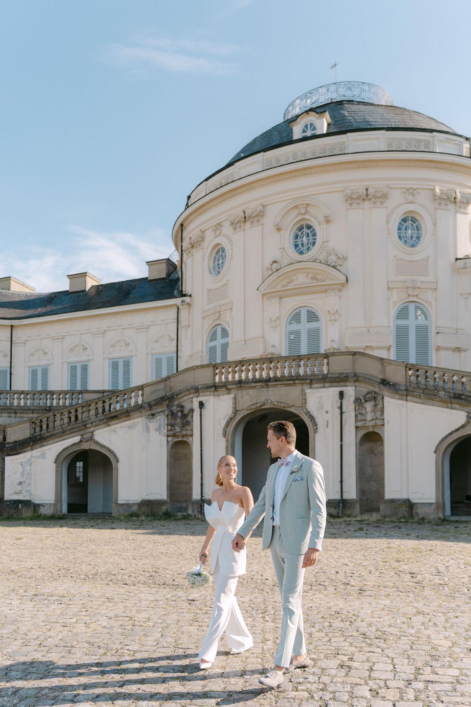 Elegant couple walks along a historic building with white stone facade and curved architecture in Stuttgart, Germany. Schloss Solitude