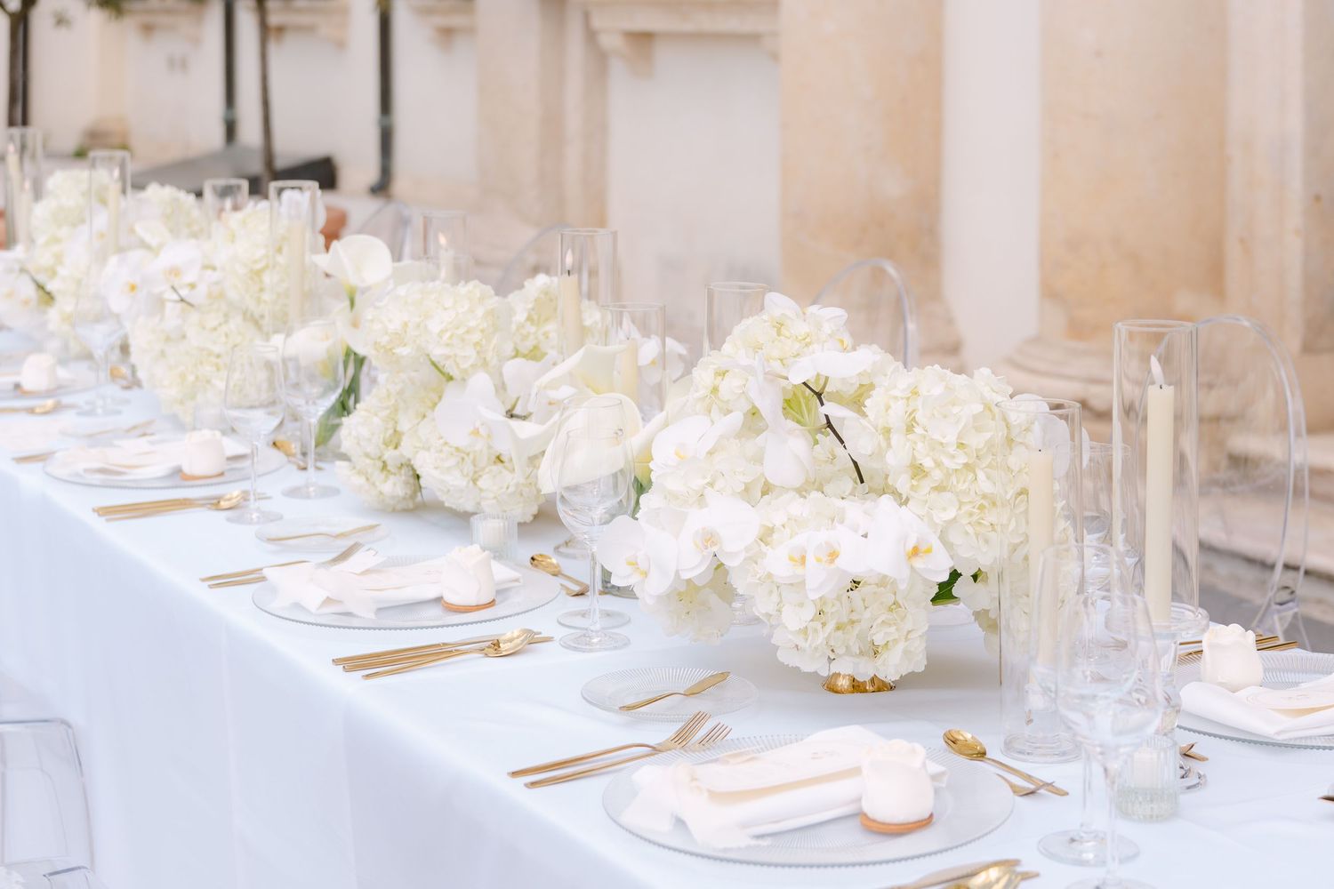 Elegant wedding reception table settings with white floral centerpieces and crystal glassware in a luxurious venue. Villa Mosconi Bertani