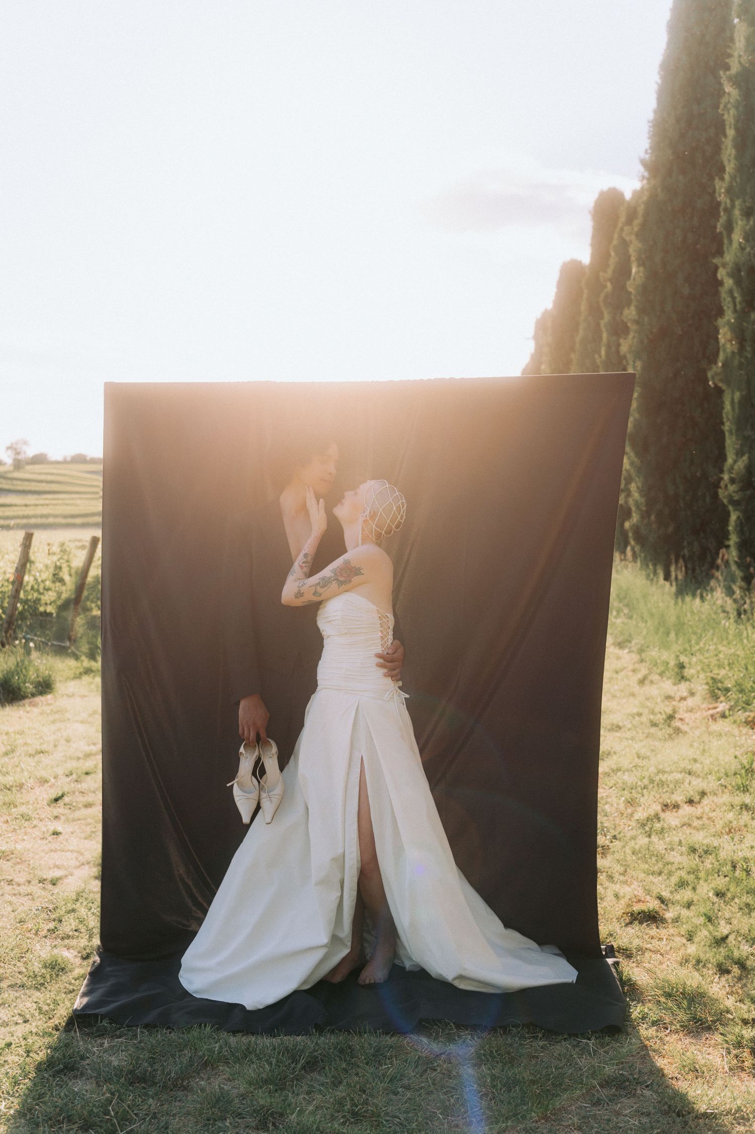 A romantic wedding photoshoot with a black backdrop against a sunlit field during golden hour.