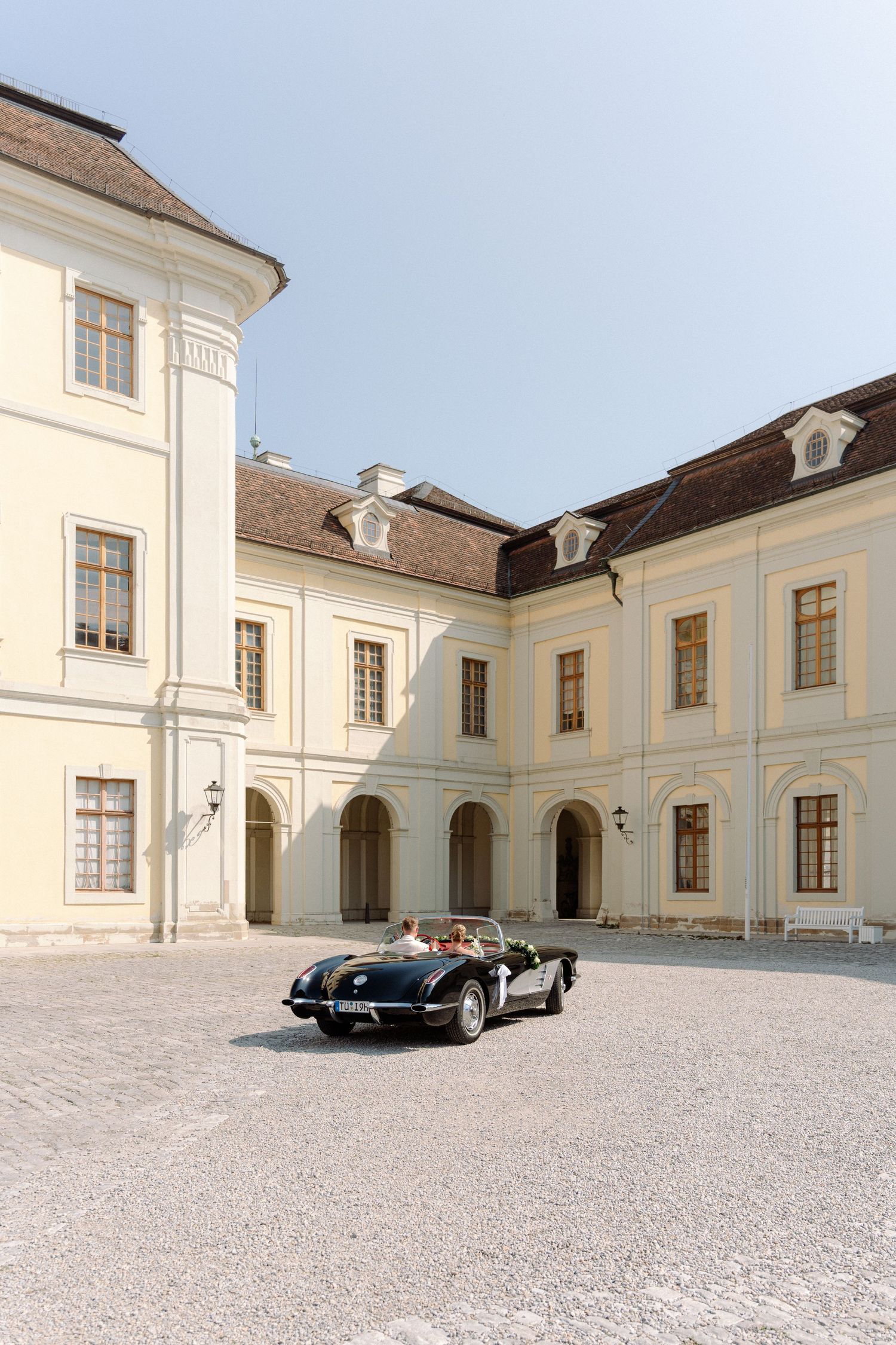 A panoramic view of a white baroque mansion courtyard with vintage black cars parked in front of the elegant facade. Schloss Ludwigsburg