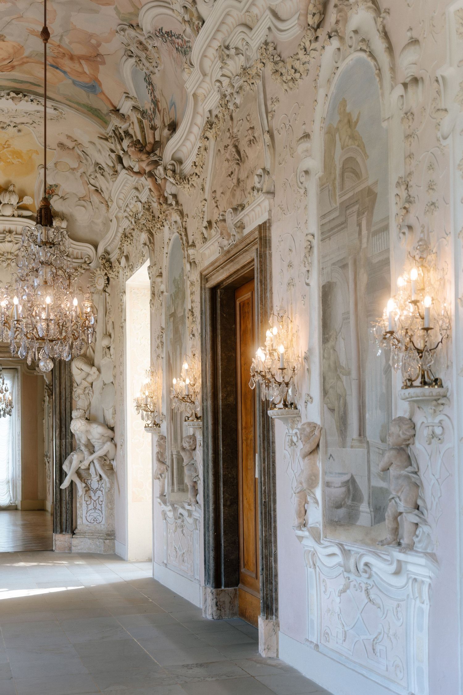 Ornate Baroque hallway with white stucco decorations, crystal chandeliers and sunlight streaming through arched windows. Schloss Ludwigsburg