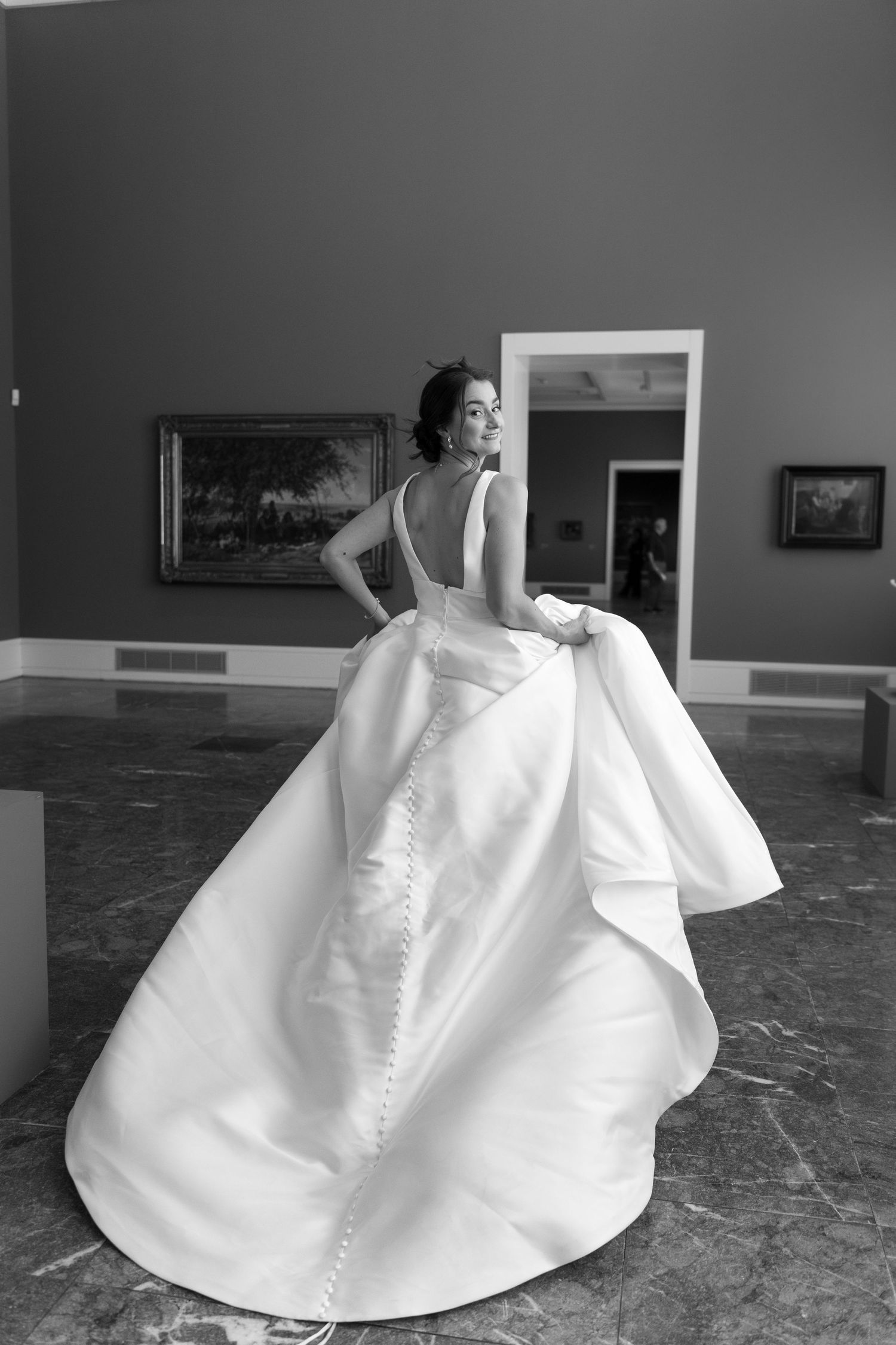 Elegant wedding gown with dramatic open back and sweeping pearl white train on marble floor shown in black and white.