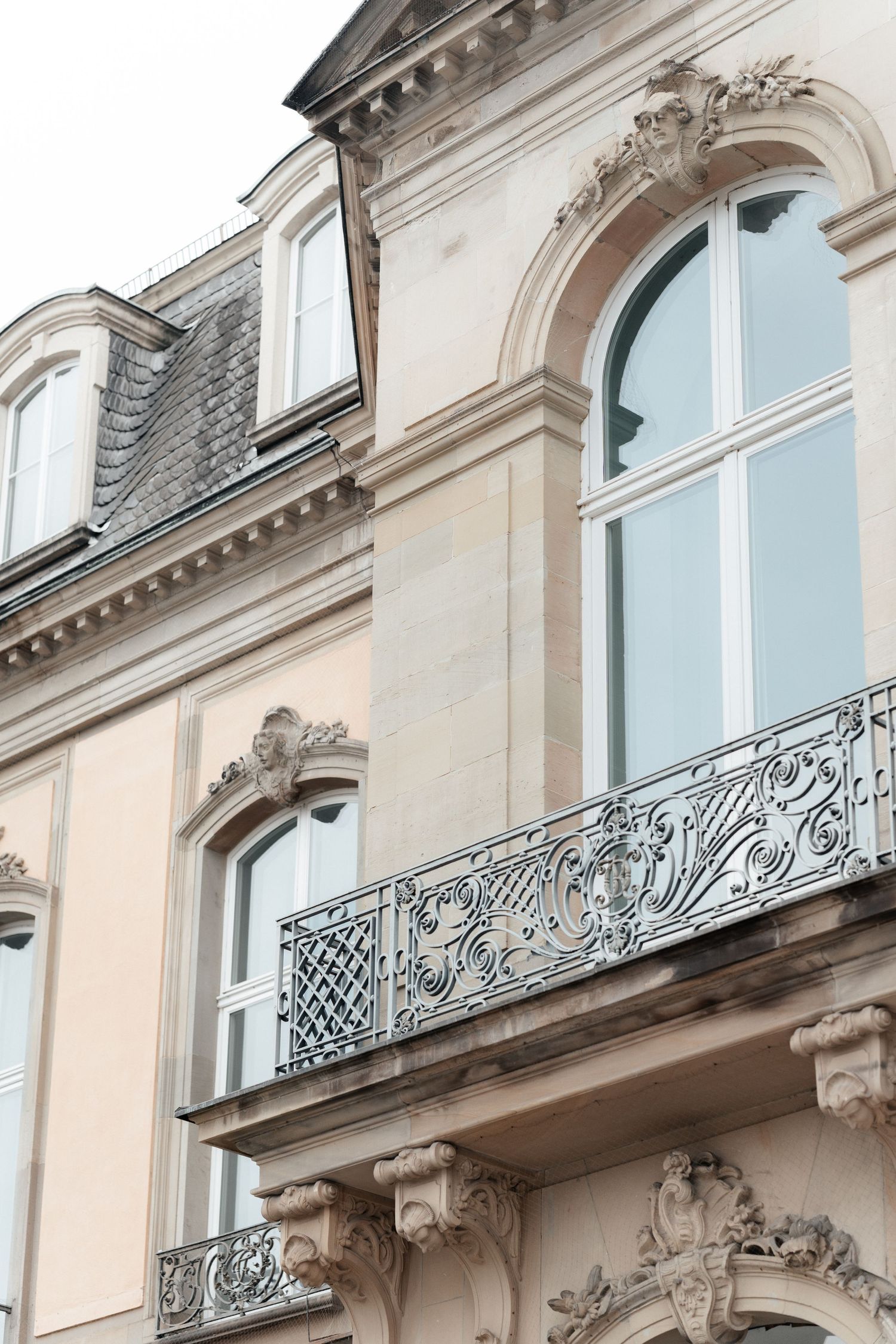 Ornate architectural details of a French building with decorative wrought iron balcony and arched windows in cream color.