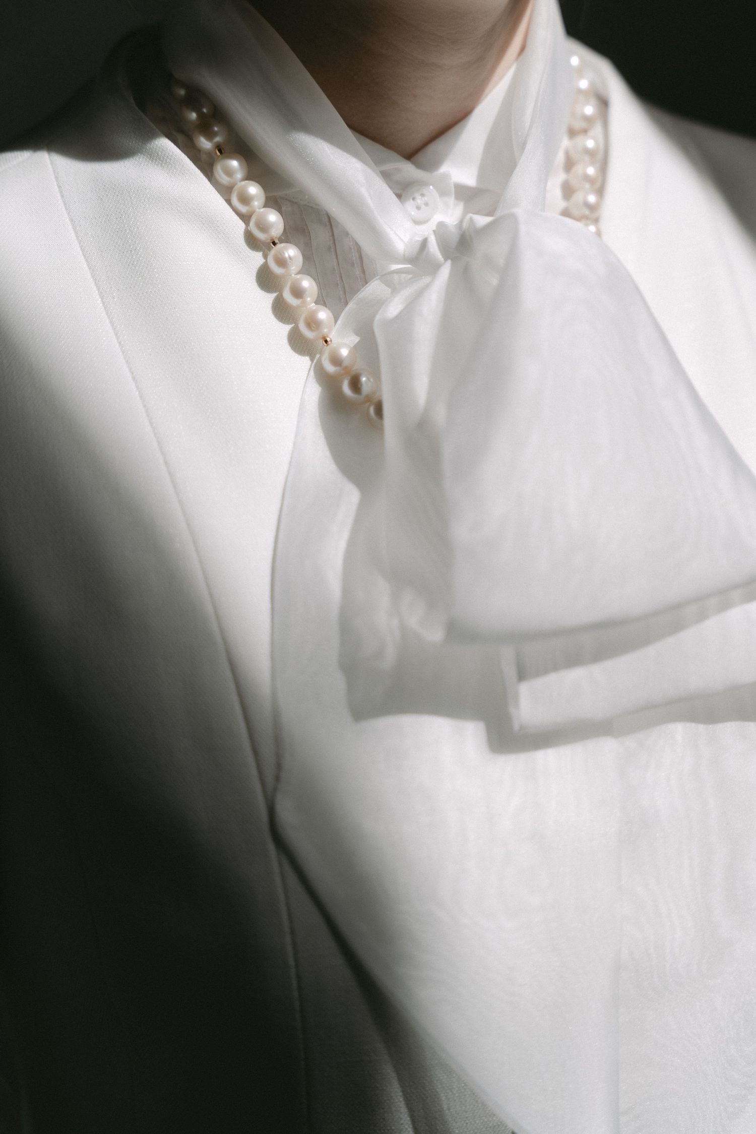 Elegant white blazer and bow blouse styled with a classic pearl necklace in a sophisticated monochromatic look.