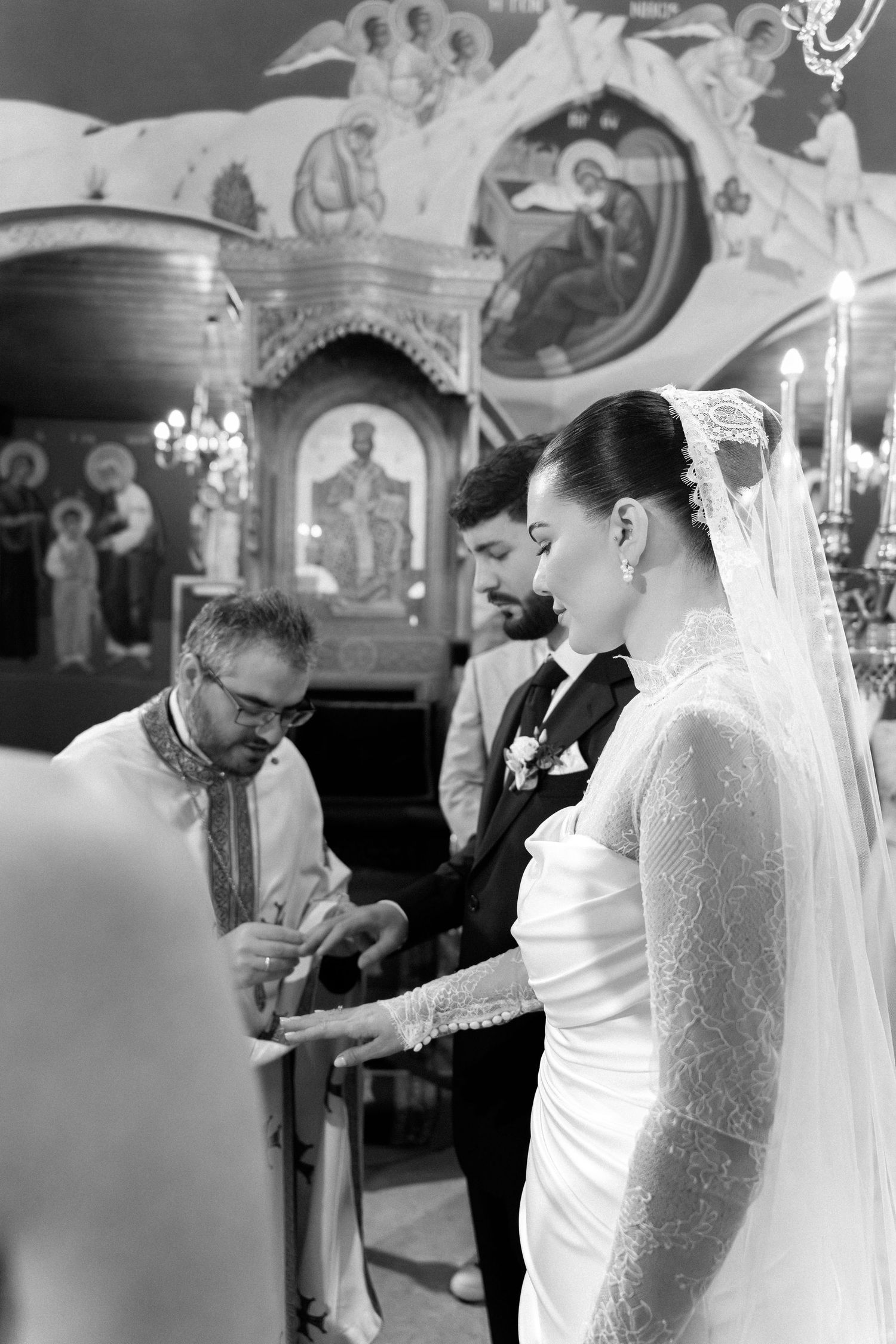 Black and white photo of a bride and groom exchanging rings during an Orthodox church wedding ceremony.