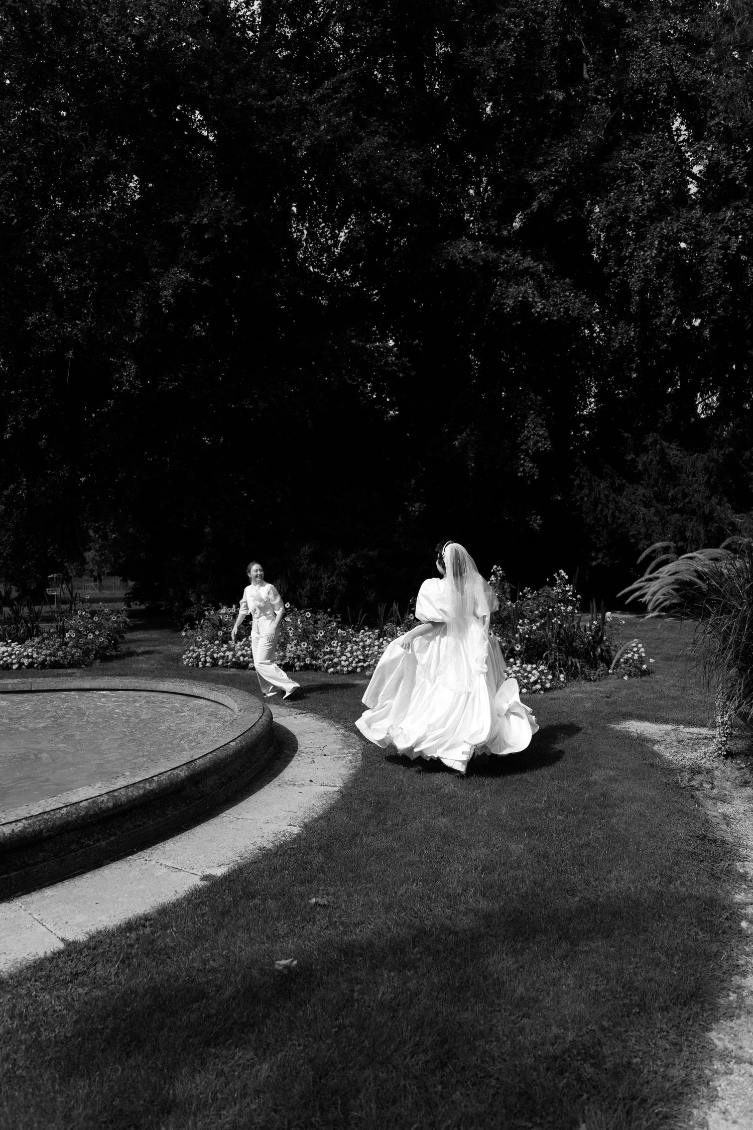 Black and white photo of a bride in a flowing white gown and veil running through a garden path.