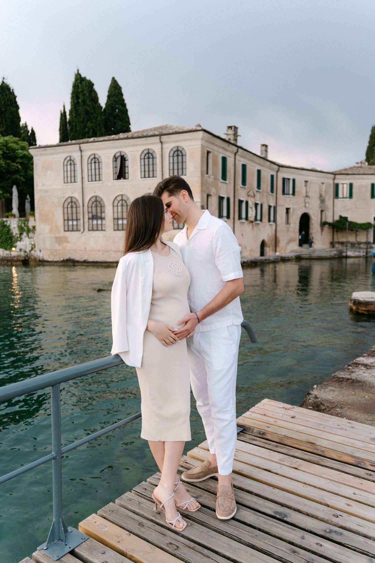A couple stands on a wooden dock overlooking historic waterfront buildings in Venice, Italy.