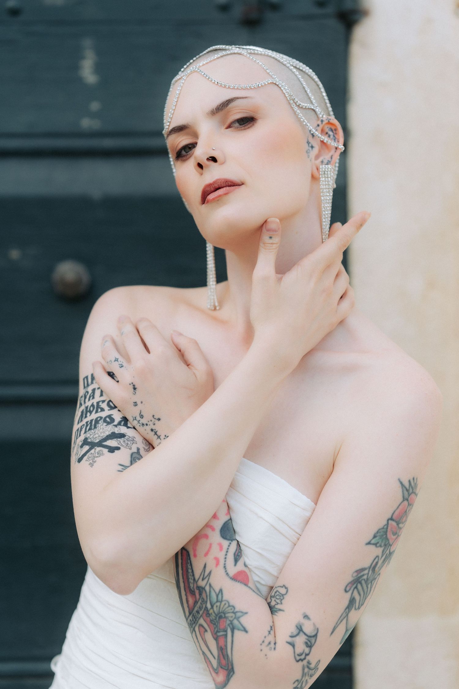 Artistic bridal portrait featuring a platinum-haired model in white dress with visible arm tattoos against teal door.
