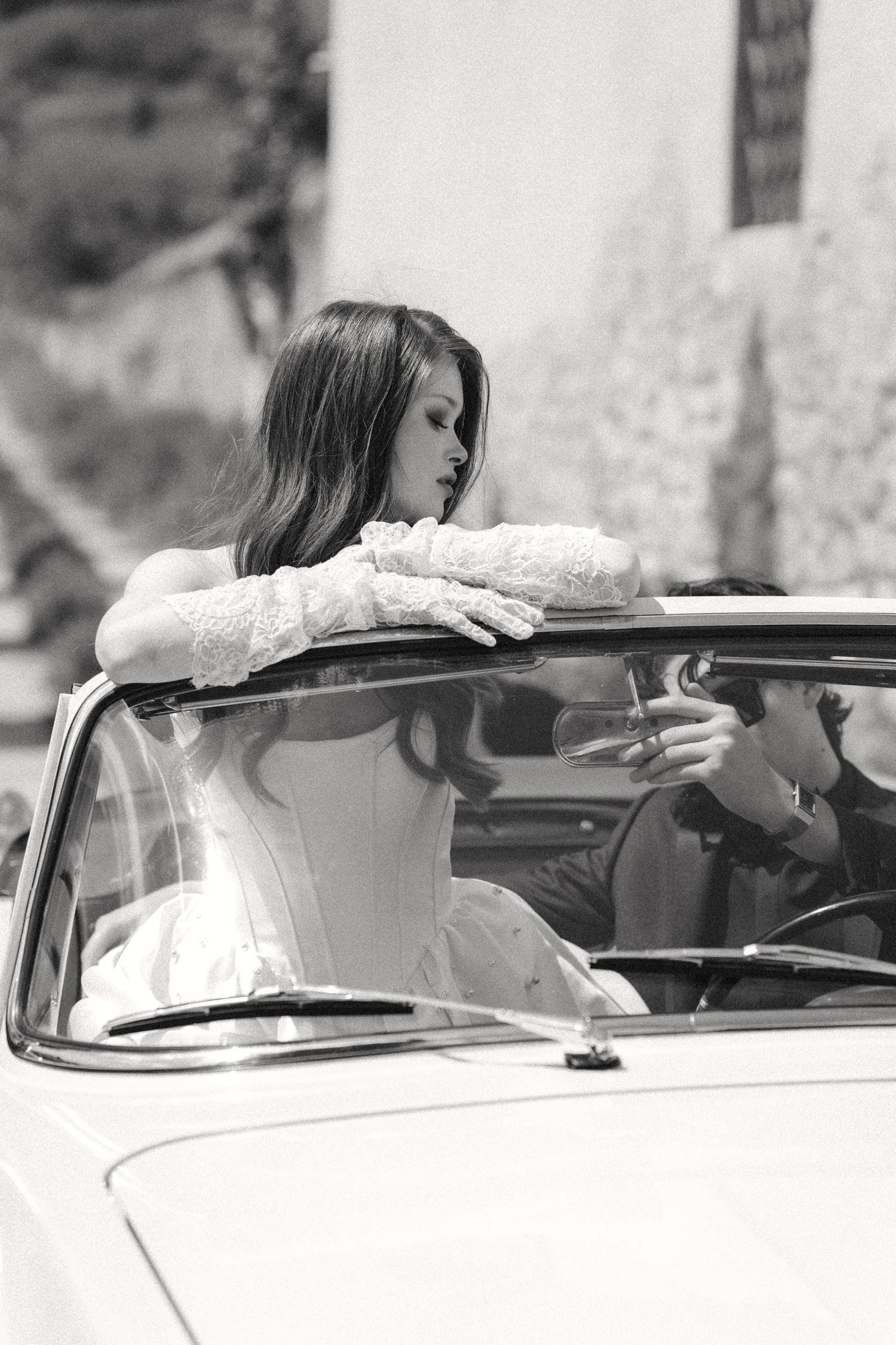 A person in a white shirt leans over a classic car in a black and white photograph series.