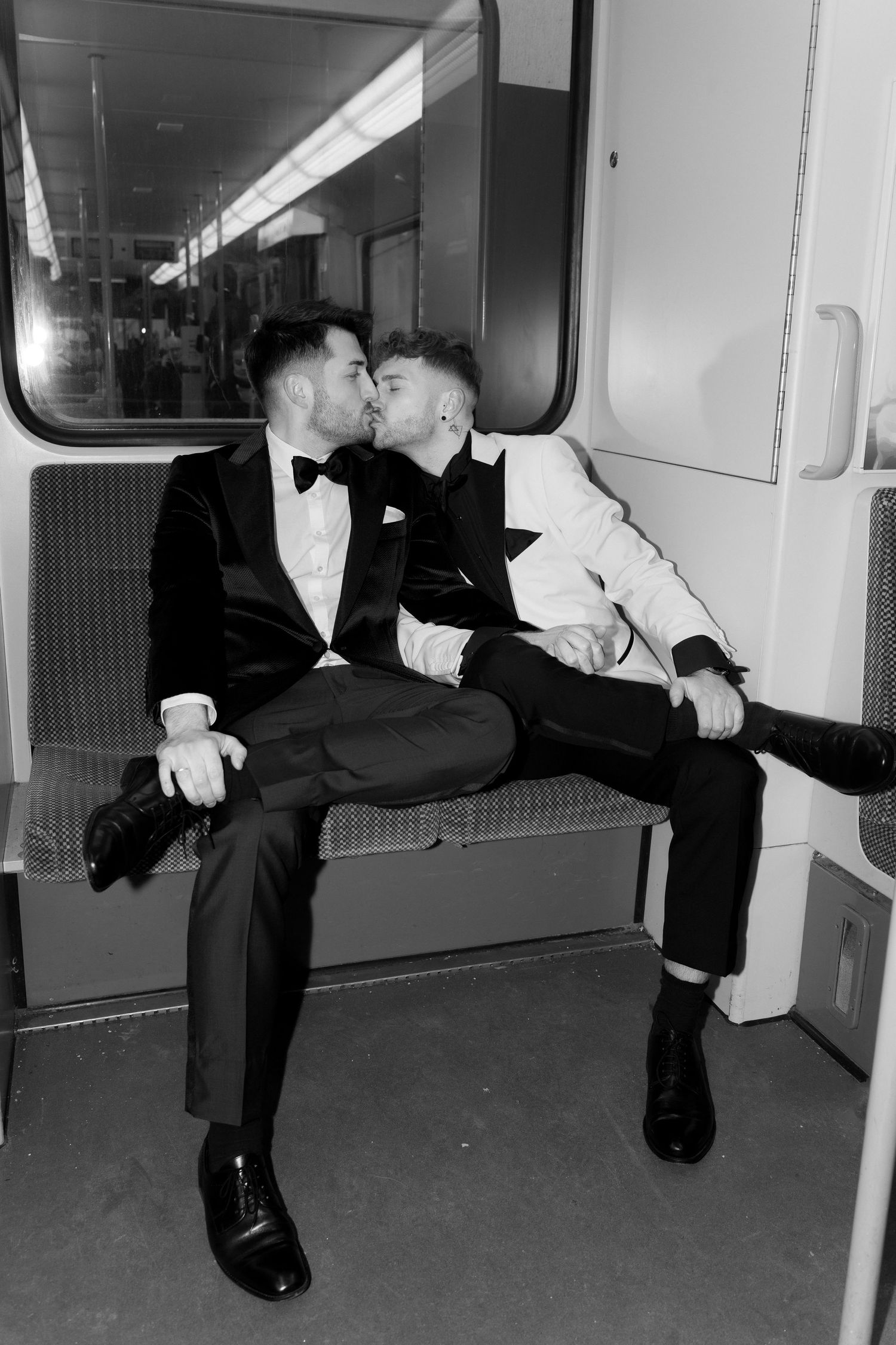 Two people in formal attire sharing an intimate moment while sitting on public transit seating.