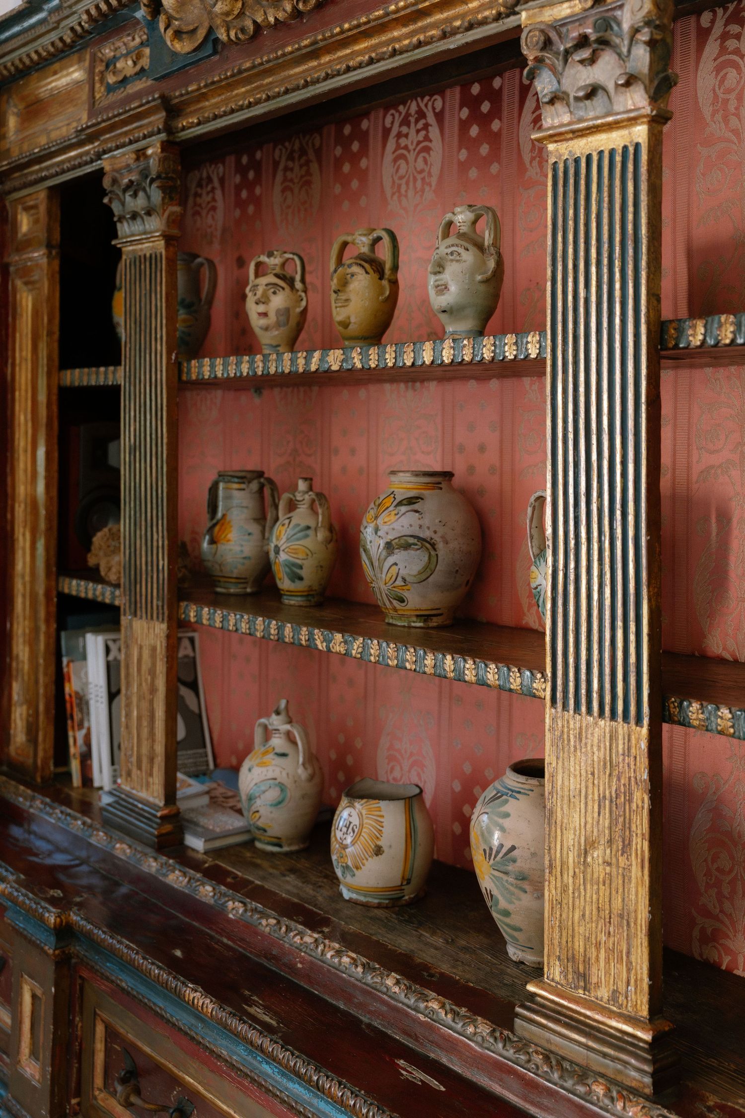 Antique wooden shelving unit displaying decorative ceramic vases and face jugs against a red painted wall.